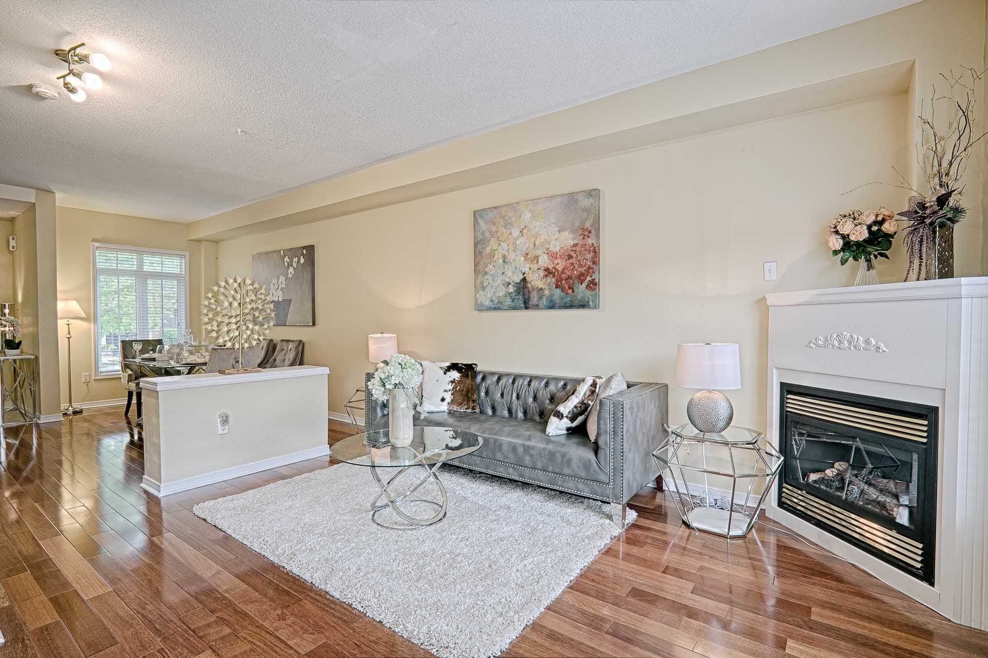 This elegant living room showcases a simple and lovely interior design with warm hardwood flooring, a cozy fireplace, and a well-balanced furniture layout. The neutral color palette, soft textures, and staged seating area create a welcoming and comfortable atmosphere. This living space emphasizes openness, functionality, and timeless style, making it ideal for modern family homes and everyday living.