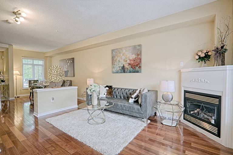 This elegant living room showcases a simple and lovely interior design with warm hardwood flooring, a cozy fireplace, and a well-balanced furniture layout. The neutral color palette, soft textures, and staged seating area create a welcoming and comfortable atmosphere. This living space emphasizes openness, functionality, and timeless style, making it ideal for modern family homes and everyday living.