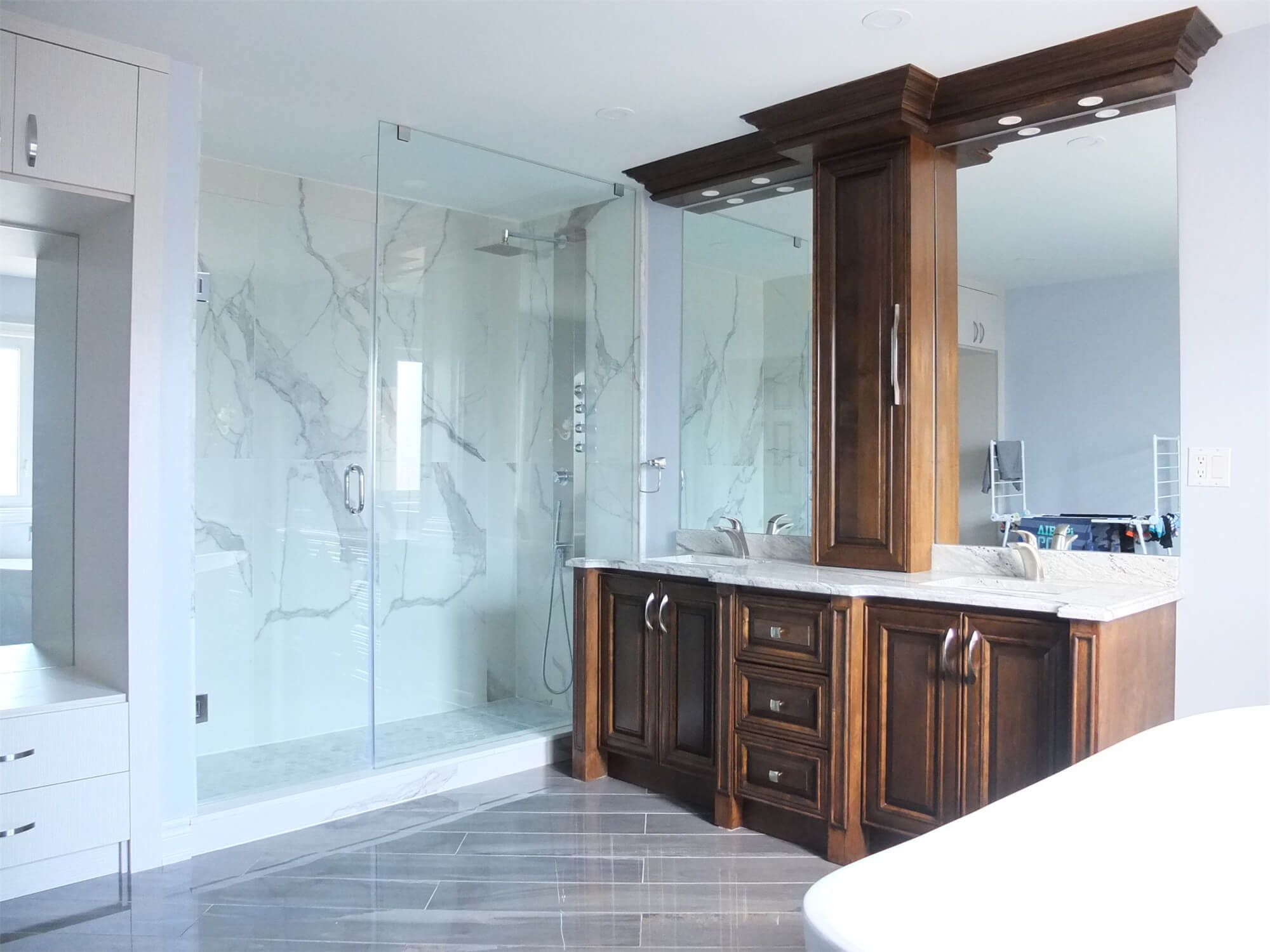 This Richmond Hill interior renovation showcases a modern luxury bathroom featuring a frameless glass walk-in shower, marble-style wall tiles, and custom solid wood vanity cabinetry with quartz countertops. The spacious layout improves functionality while maintaining an elegant and timeless design. Large mirrors, upgraded lighting, and durable floor tiles enhance both comfort and usability for daily living. Completed by a professional Toronto renovation company, this bathroom renovation combines high-end finishes with practical design to increase home value and long-term performance.