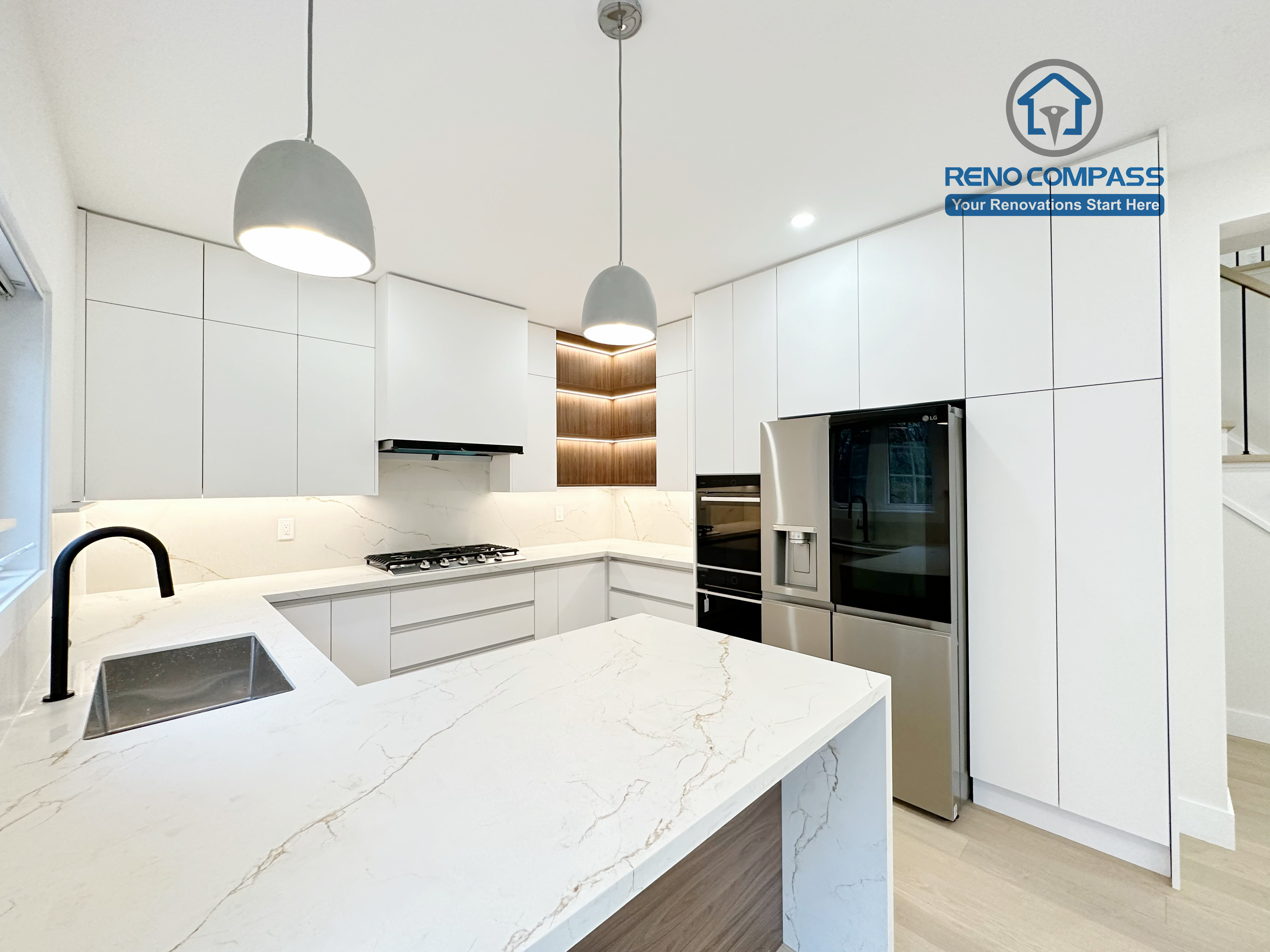 This image presents a modern kitchen renovation in Richmond Hill featuring full-height custom white cabinetry, a quartz waterfall island with wood panel detailing, and integrated stainless steel appliances. The design includes a built-in gas cooktop, minimalist pendant lights, recessed ceiling lighting, and light hardwood flooring for a clean, contemporary look. Large windows and patio access enhance natural light and openness. Completed by a professional Toronto Renovation Company, this kitchen renovation reflects refined craftsmanship, efficient layout planning, and modern family-focused design.