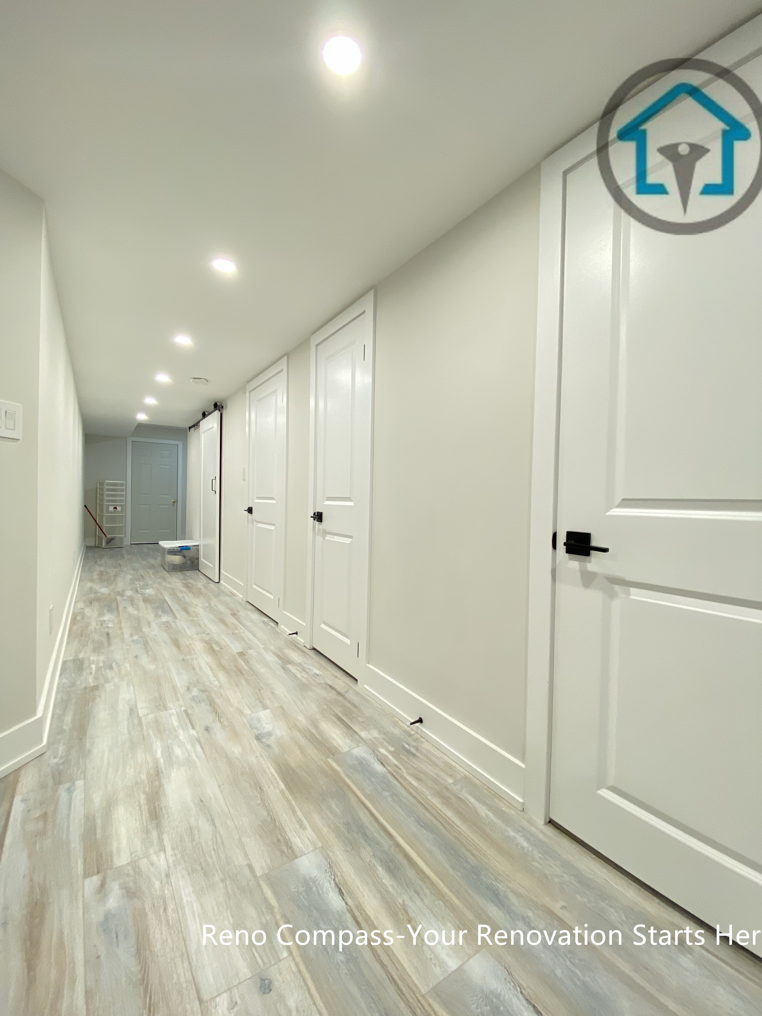 This Stouffville basement renovation features a long hallway with newly installed vinyl plank flooring, recessed ceiling lighting, and modern interior doors with black hardware. The clean lines and neutral tones improve brightness, circulation, and overall usability, creating a well-connected basement layout completed by Reno Compass Inc.