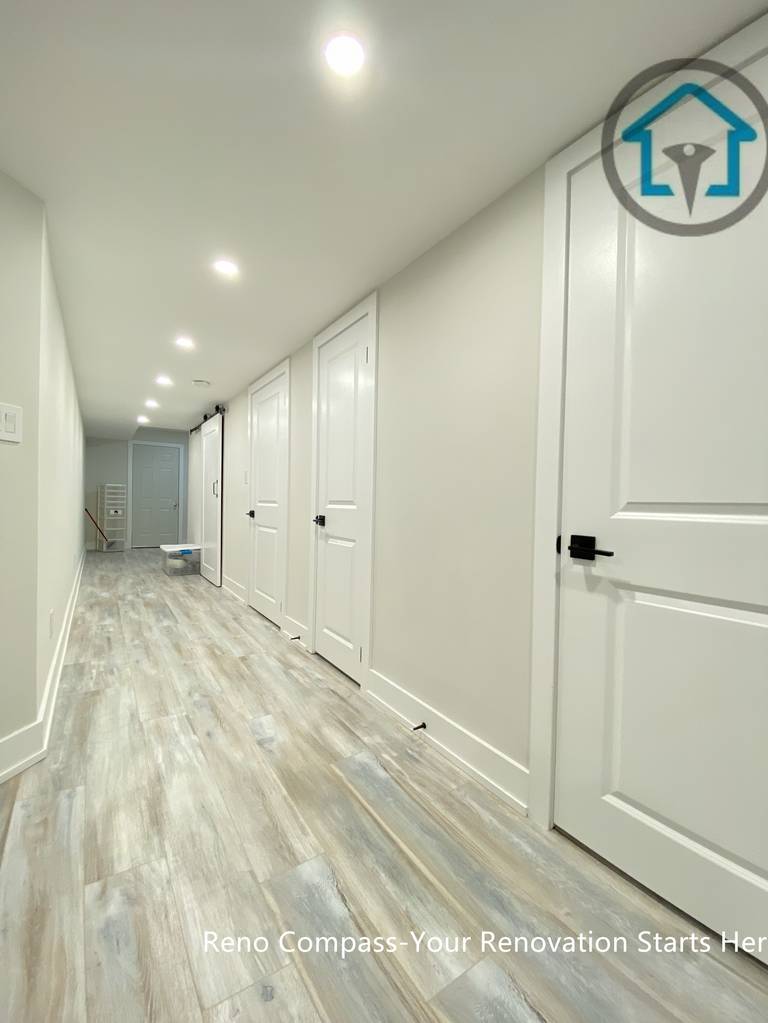 This Stouffville basement renovation features a long hallway with newly installed vinyl plank flooring, recessed ceiling lighting, and modern interior doors with black hardware. The clean lines and neutral tones improve brightness, circulation, and overall usability, creating a well-connected basement layout completed by Reno Compass Inc.