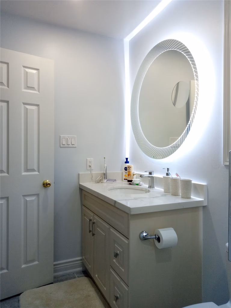 This image showcases a renovated bathroom vanity as part of a Richmond Hill basement and upper floor bathroom renovation project. The space features a modern vanity cabinet, updated countertop, and a round LED backlit mirror that enhances lighting and visual depth. Clean finishes and efficient layout improve both functionality and aesthetics, reflecting the attention to detail and craftsmanship of a professional Toronto renovation company.