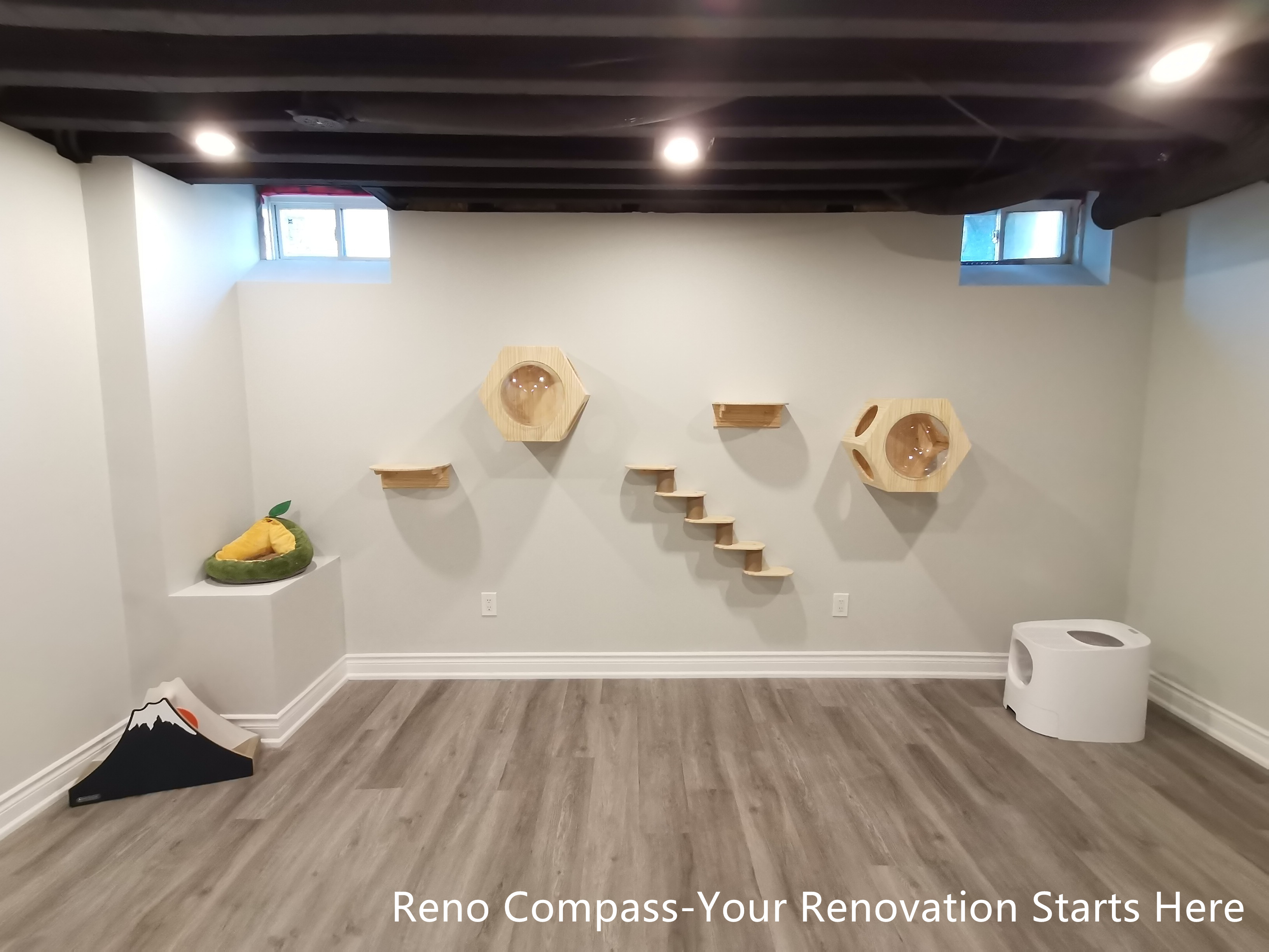 This image highlights a custom-designed cat activity wall within an industrial-style basement renovation in Vaughan. The sprayed black open ceiling and recessed lighting create a strong architectural backdrop, while wall-mounted platforms and enclosed cat pods are arranged in a balanced, linear composition. The design allows pets to climb, rest, and move freely without interrupting the clarity of the space. Combined with durable flooring and neutral wall finishes, the basement achieves a clean, organized, and pet-friendly environment. Designed and completed by Reno Compass, this renovation reflects thoughtful customization integrated seamlessly into a functional living space.