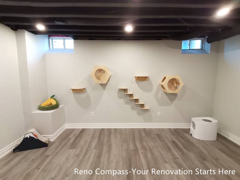 This image highlights a custom-designed cat activity wall within an industrial-style basement renovation in Vaughan. The sprayed black open ceiling and recessed lighting create a strong architectural backdrop, while wall-mounted platforms and enclosed cat pods are arranged in a balanced, linear composition. The design allows pets to climb, rest, and move freely without interrupting the clarity of the space. Combined with durable flooring and neutral wall finishes, the basement achieves a clean, organized, and pet-friendly environment. Designed and completed by Reno Compass, this renovation reflects thoughtful customization integrated seamlessly into a functional living space.