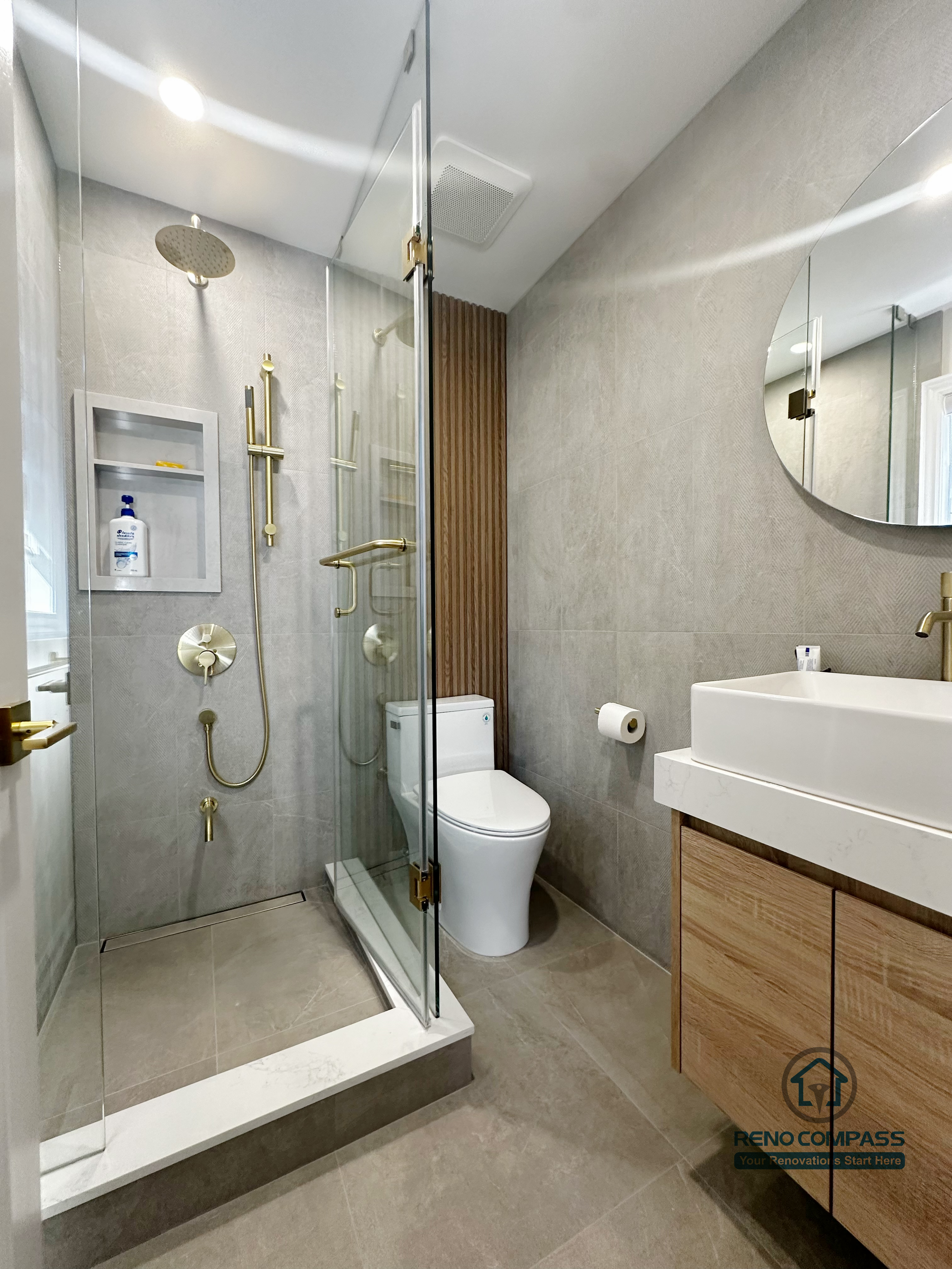This North York bathroom renovation features a custom walk-in glass shower with built-in niche shelving, gold shower fixtures, and large-format grey tiles. A floating wood vanity and minimalist layout enhance both functionality and modern visual appeal, creating a refined spa-inspired bathroom space.