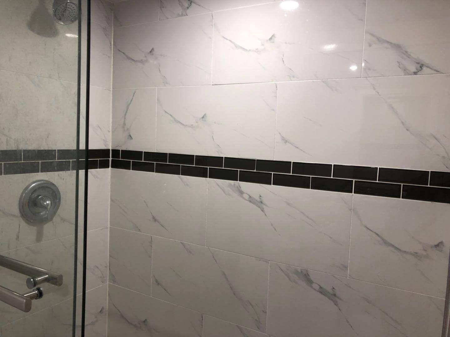 Custom shower installation as part of a Toronto basement renovation project, featuring marble-look porcelain wall tiles, black accent strip detailing, frameless glass enclosure, and modern chrome fixtures for a clean and contemporary finish.