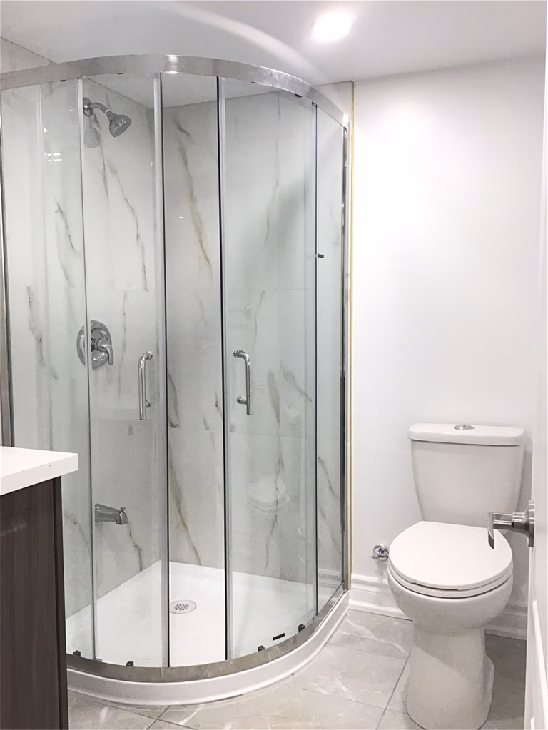 This Mississauga basement bathroom renovation features a sleek curved glass shower enclosure, marble-style wall panels, and modern fixtures. The clean and compact design maximizes space while maintaining a bright and elegant look, perfect for a basement suite or guest bathroom.