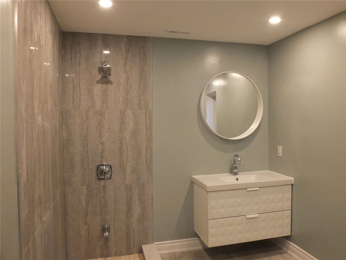 This image features a modern bathroom renovation completed as part of a Mississauga interior renovation project. The design includes a walk-in tiled shower with full-height wall tiles, recessed ceiling lighting, and a sleek floating vanity paired with a round mirror. Neutral wall colors and clean lines create a bright, minimalist atmosphere while maximizing functionality and comfort. Completed by an experienced Toronto renovation company, this bathroom renovation improves daily usability, moisture resistance, and overall interior value for homeowners in Mississauga and the Greater Toronto Area.