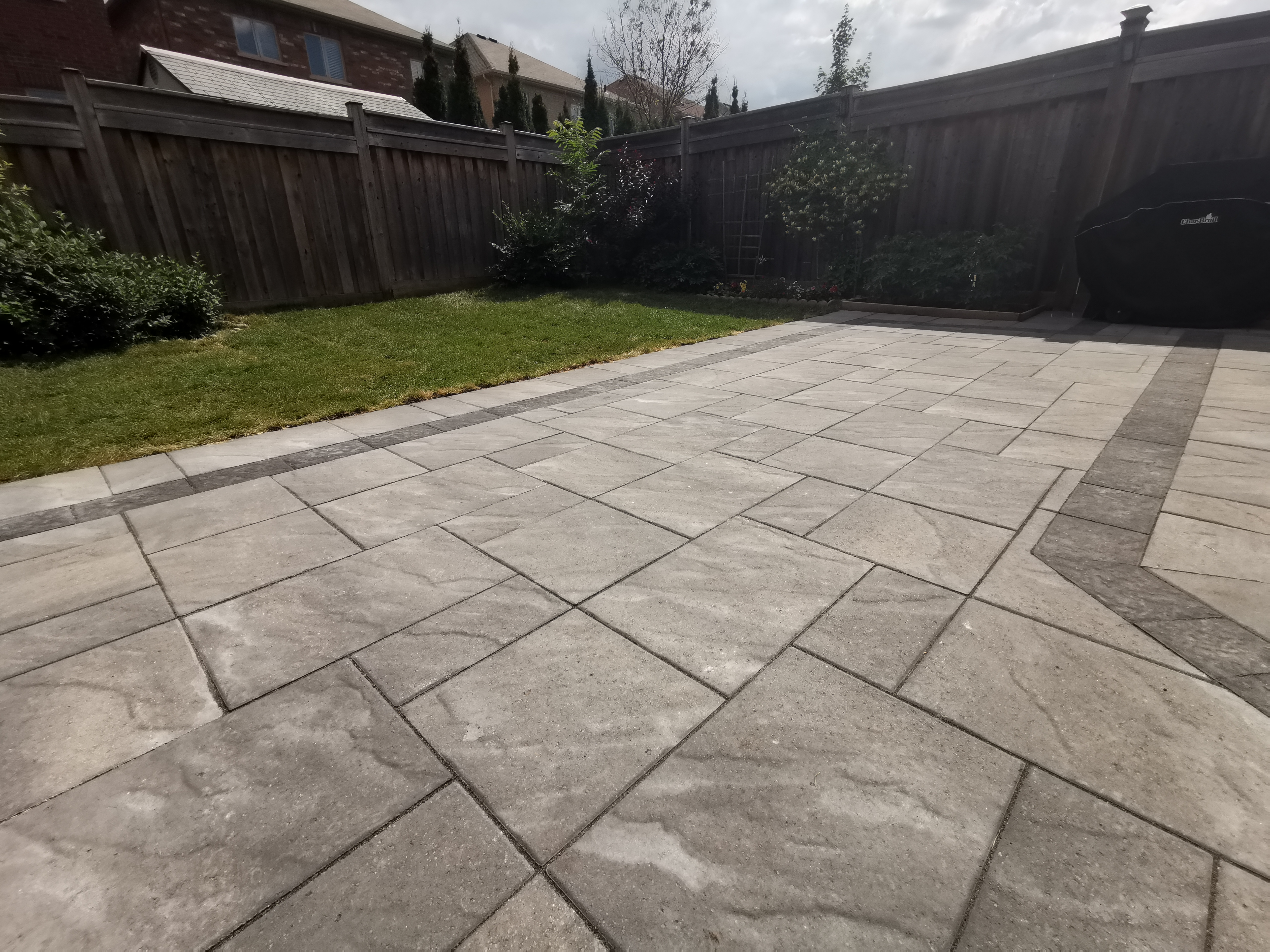 This Aurora backyard interlocking paver patio is designed to create a functional and inviting outdoor living space. Large-format concrete pavers are installed in a clean linear pattern with a contrasting border, enhancing visual definition and long-term durability. The patio seamlessly connects to a raised wooden deck with integrated steps, allowing smooth movement between indoor and outdoor areas. This professionally built interlock patio offers excellent drainage, stability, and low maintenance, making it ideal for family use and everyday enjoyment in residential backyards across Aurora.