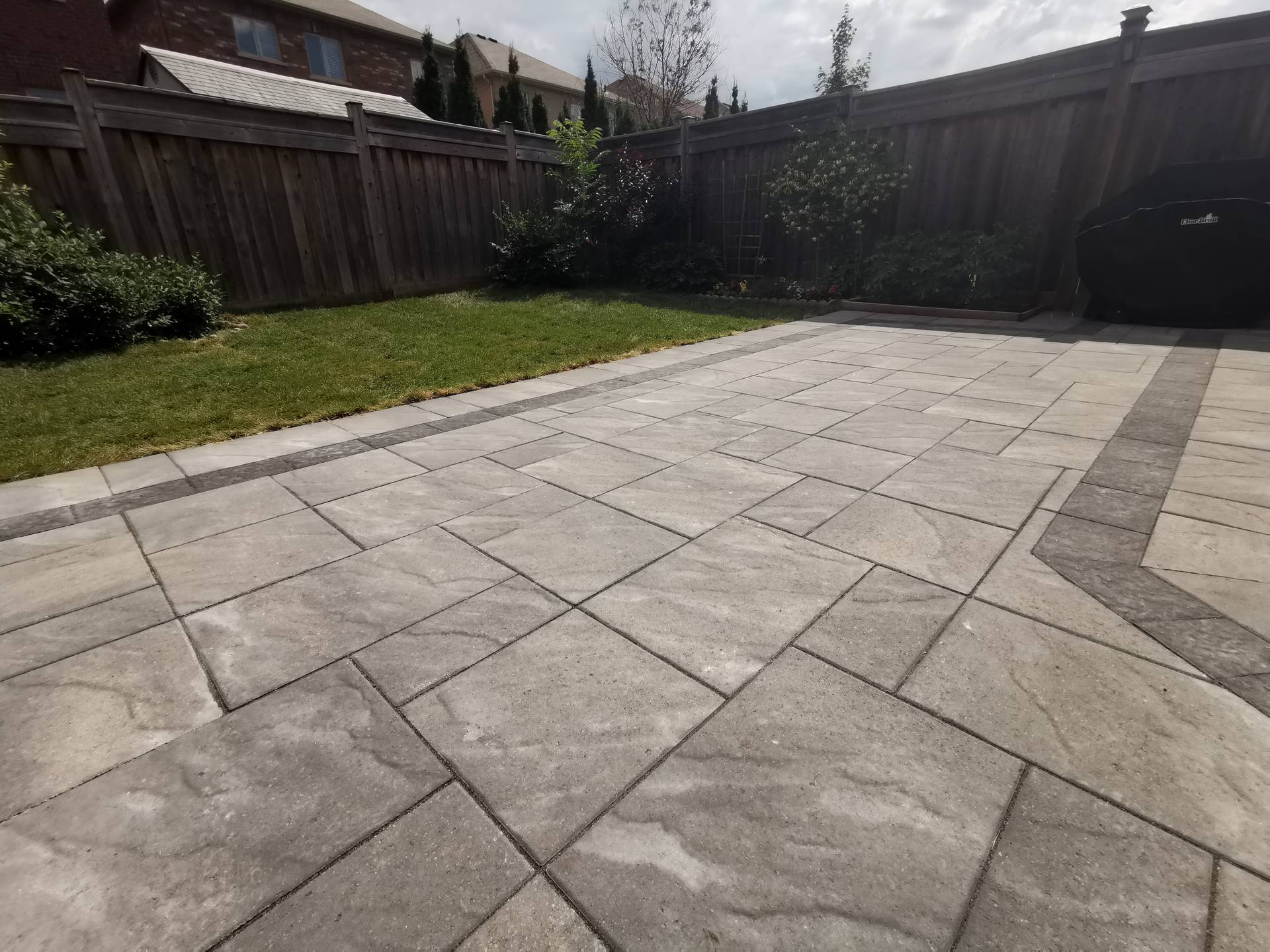 This Aurora backyard interlocking paver patio is designed to create a functional and inviting outdoor living space. Large-format concrete pavers are installed in a clean linear pattern with a contrasting border, enhancing visual definition and long-term durability. The patio seamlessly connects to a raised wooden deck with integrated steps, allowing smooth movement between indoor and outdoor areas. This professionally built interlock patio offers excellent drainage, stability, and low maintenance, making it ideal for family use and everyday enjoyment in residential backyards across Aurora.