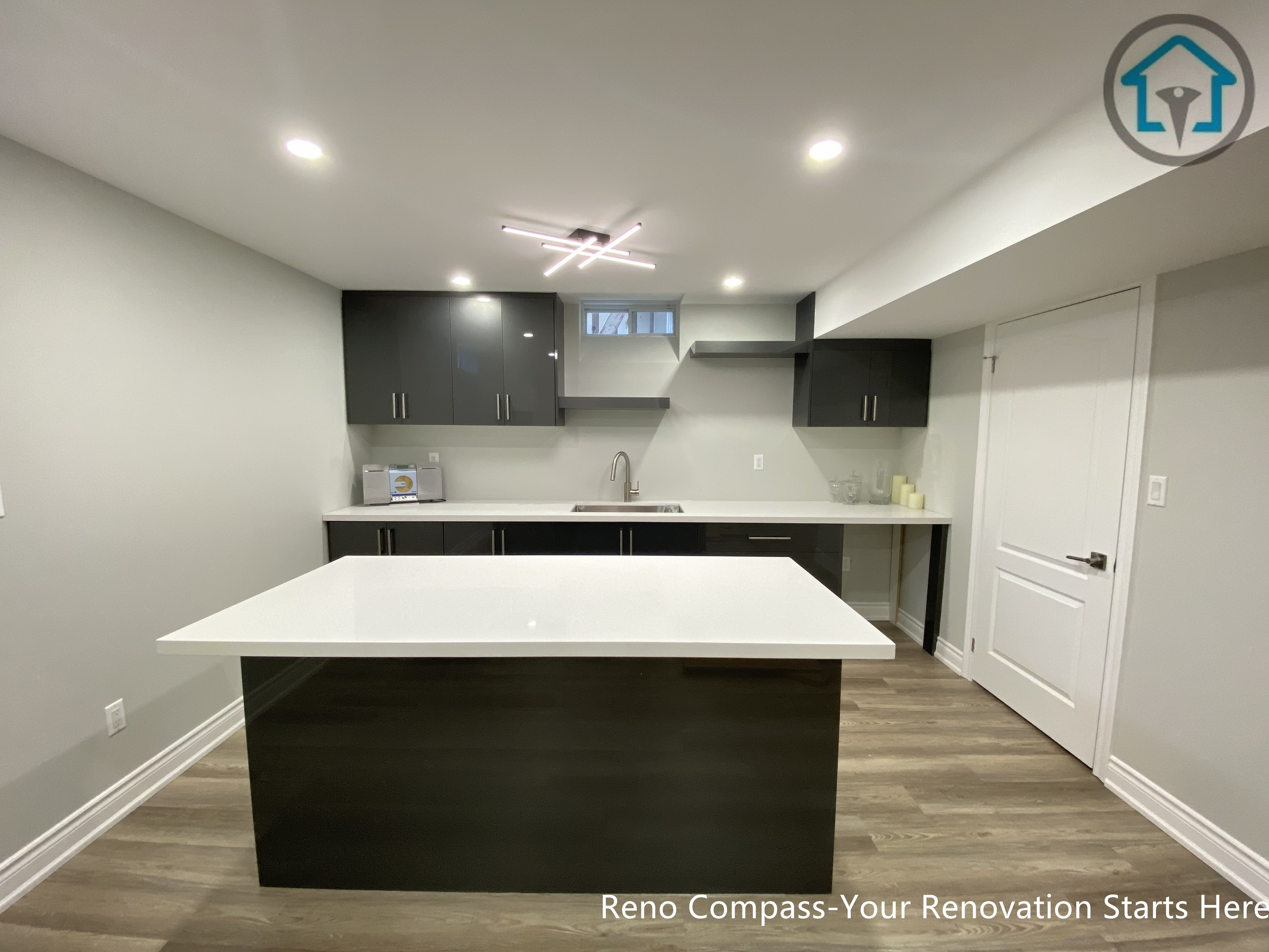 A modern basement kitchen renovation in Markham featuring a large quartz island, custom dark cabinetry, integrated lighting, and durable flooring, creating a functional and stylish lower-level living space.
