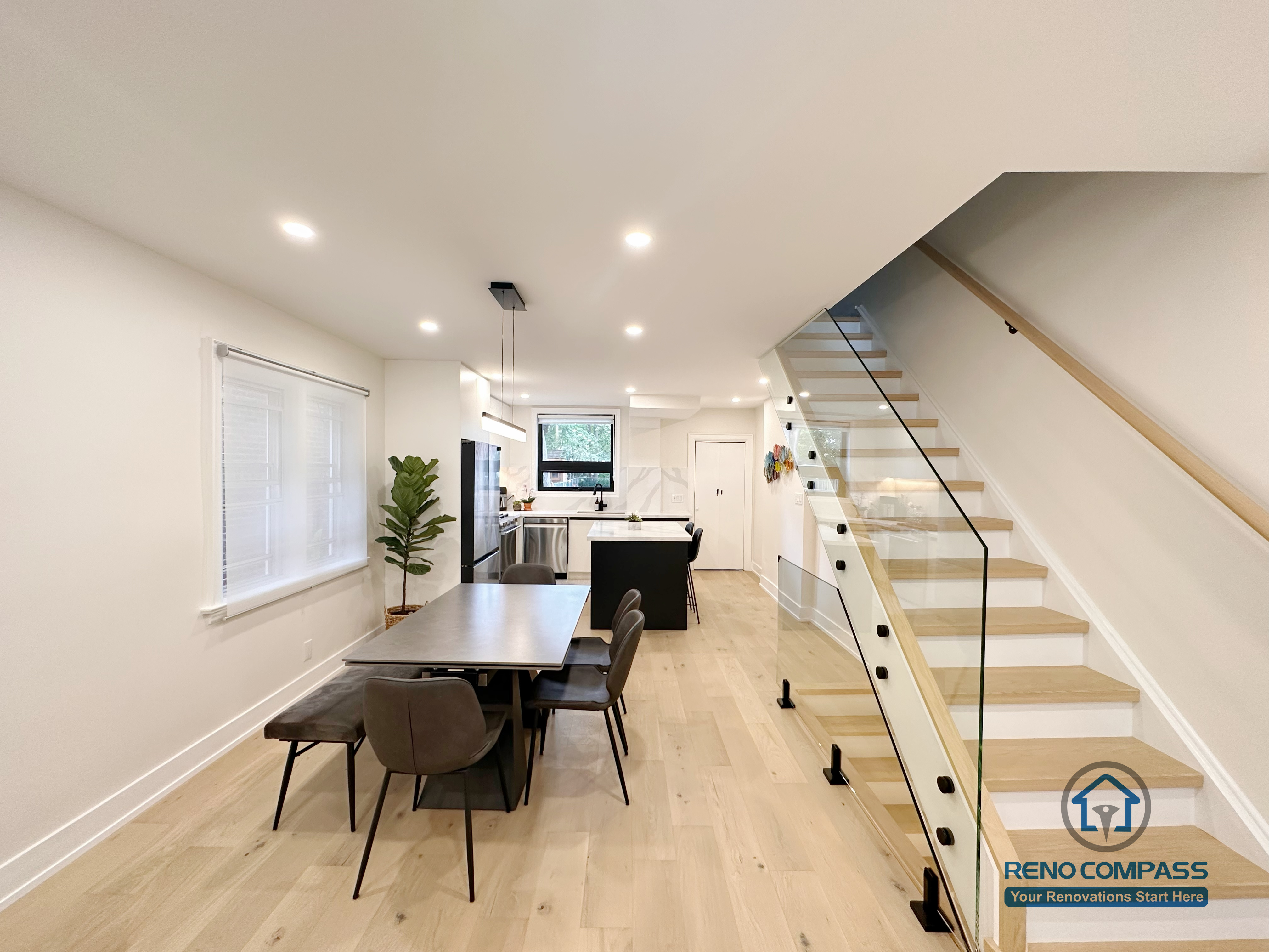 This Toronto interior renovation features a bright open-concept layout with a modern dining area, custom kitchen island, wide-plank hardwood flooring, and a sleek glass staircase. The design maximizes natural light and creates a seamless flow between dining, kitchen, and living spaces, showcasing contemporary craftsmanship by a professional Toronto renovation company.