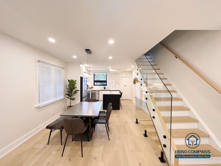 This Toronto interior renovation features a bright open-concept layout with a modern dining area, custom kitchen island, wide-plank hardwood flooring, and a sleek glass staircase. The design maximizes natural light and creates a seamless flow between dining, kitchen, and living spaces, showcasing contemporary craftsmanship by a professional Toronto renovation company.