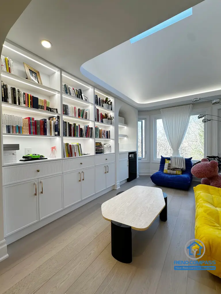 This area of the Markham interior renovation was designed as a calm, functional lounge that combines custom storage with everyday comfort. Full-height built-in shelving along one wall provides organized space for books and personal items while maintaining a clean, integrated appearance within the room.

The ceiling design features recessed lighting and soft indirect illumination, creating an even and inviting atmosphere without visual clutter. Light wood flooring helps balance the white cabinetry and bright furnishings, ensuring the space feels warm rather than overly minimal.

Designed for reading, relaxation, and quiet family time, this lounge area reflects a thoughtful approach to interior planning—where storage, lighting, and comfort work together to support daily living.