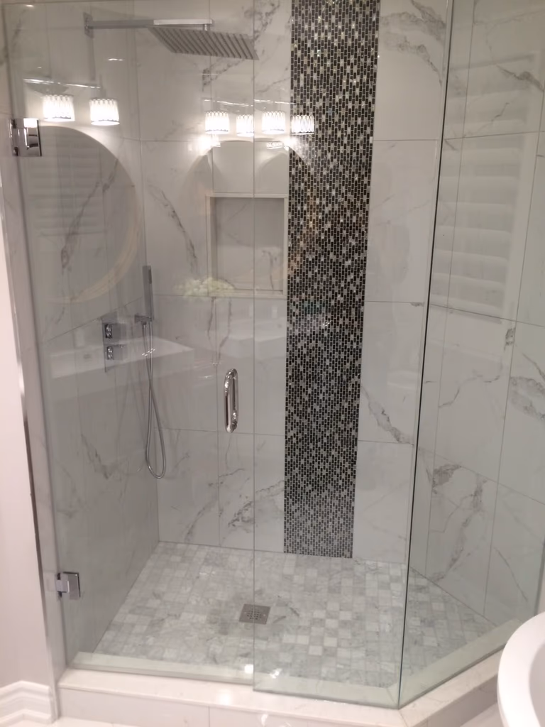 This Toronto bathroom renovation showcases a modern glass shower installation designed to enhance both functionality and contemporary style. The frameless glass enclosure creates a clean, open look while maximizing light and visual space within the bathroom.

Large-format marble-look tiles and a contrasting mosaic feature strip add depth and texture, creating a sophisticated focal point inside the shower area. The built-in wall niche provides convenient storage for daily essentials, while the rainfall showerhead and handheld fixture improve comfort and usability.

Completed by a professional Toronto renovation company, this bathroom upgrade highlights detailed tile work, precise glass installation, and high-quality waterproofing to ensure long-term durability. The result is a sleek, modern shower space that elevates both everyday comfort and overall home value.