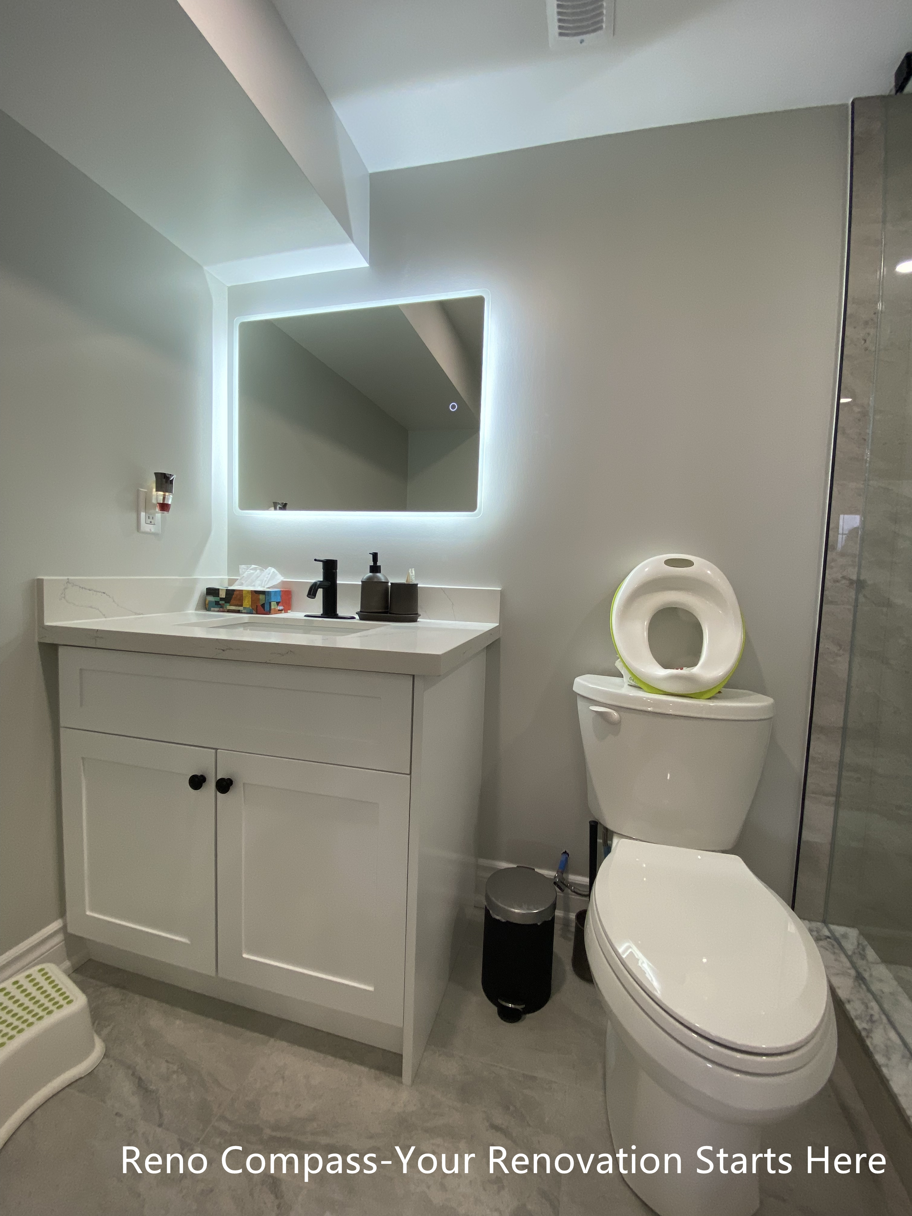 Basement bathroom vanity renovation in Oakville featuring a custom white shaker vanity with quartz countertop, LED backlit mirror, matte black faucet, and a compact, efficient layout designed to maximize functionality in a basement space, completed by Reno Compass Inc.