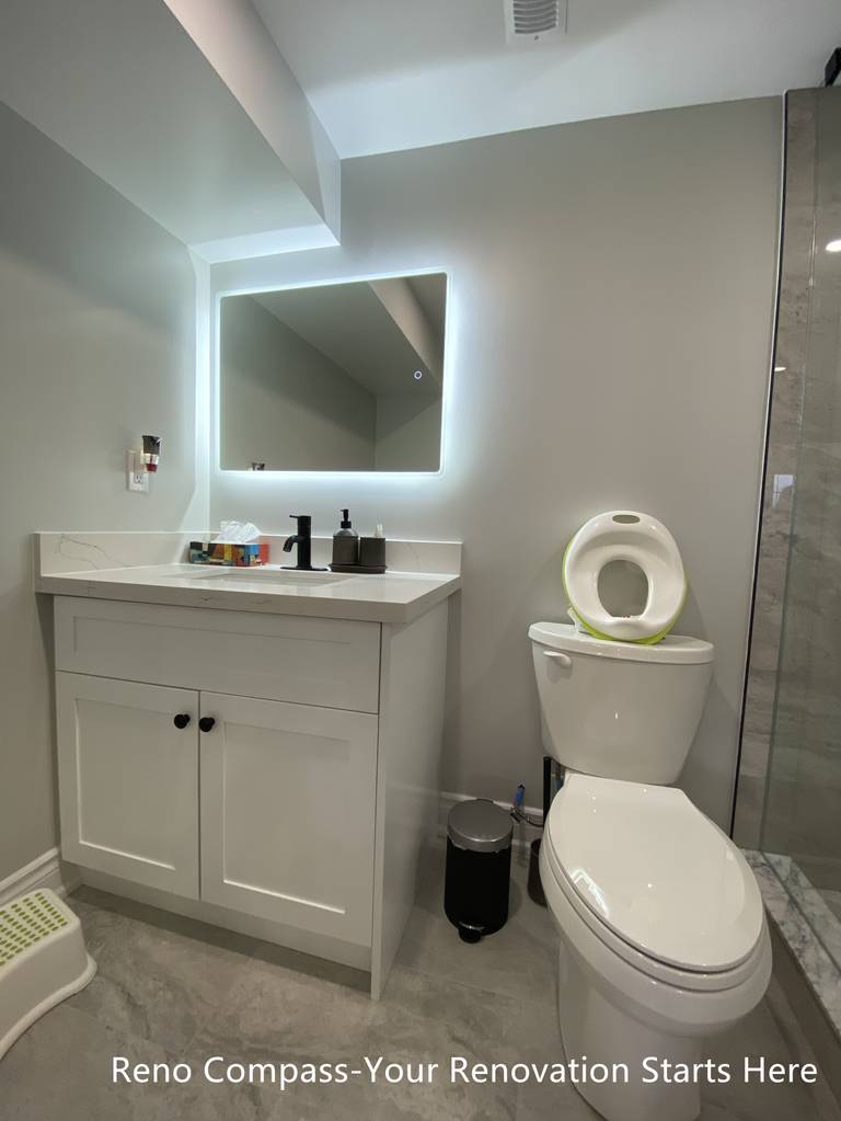 Basement bathroom vanity renovation in Oakville featuring a custom white shaker vanity with quartz countertop, LED backlit mirror, matte black faucet, and a compact, efficient layout designed to maximize functionality in a basement space, completed by Reno Compass Inc.