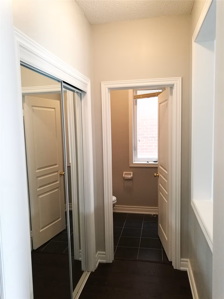 This image showcases a hallway and bathroom entrance after a Markham interior renovation, featuring clean wall finishes, upgraded doors, mirrored closet storage, and dark tile flooring that improves daily circulation and space efficiency.