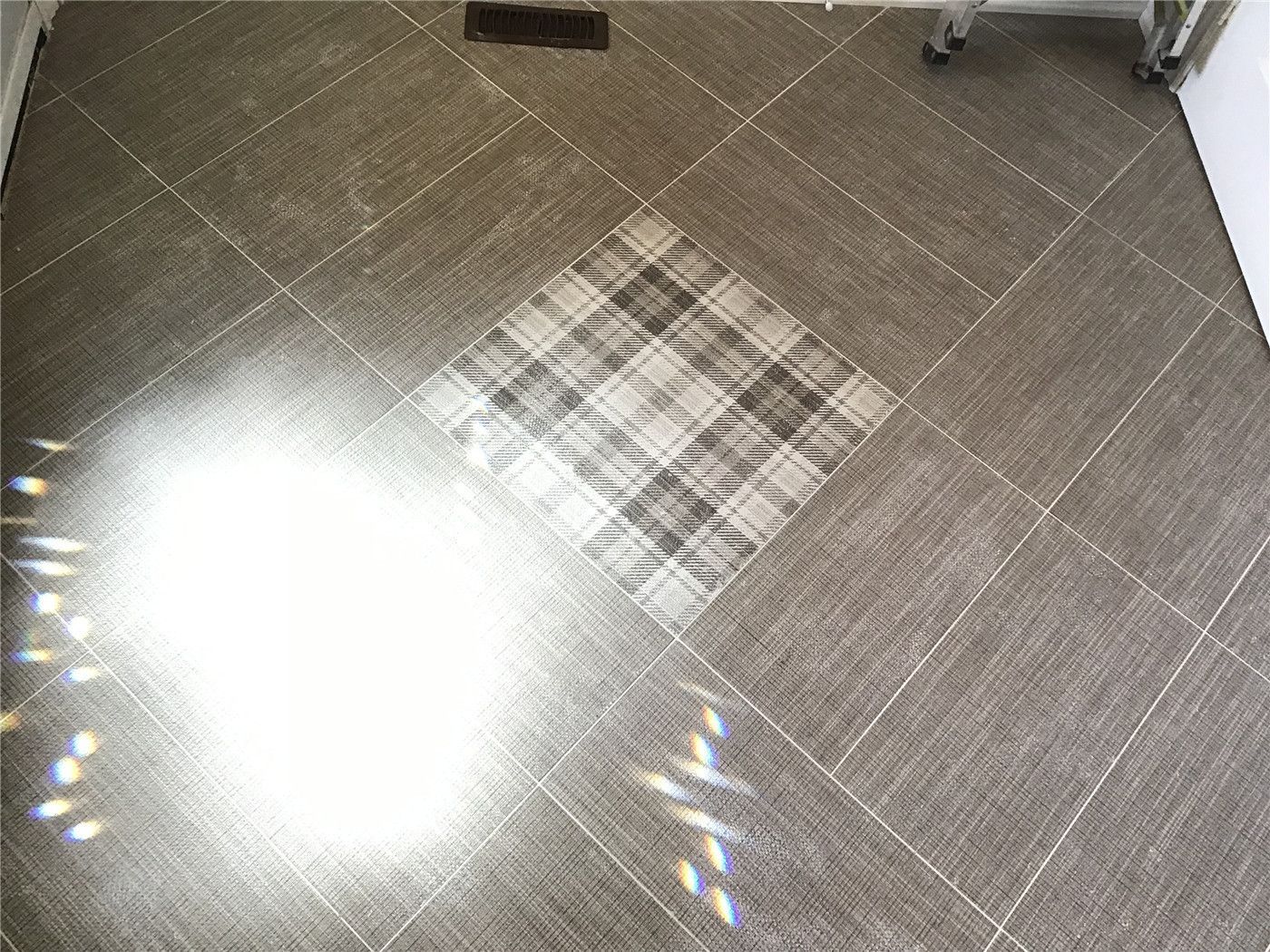This Woodbridge interior renovation showcases durable grey porcelain floor tiles installed in a clean grid layout, enhanced by a decorative center inlay detail. The design adds visual interest while maintaining a modern and low-maintenance flooring solution, ideal for high-traffic kitchen or living areas.