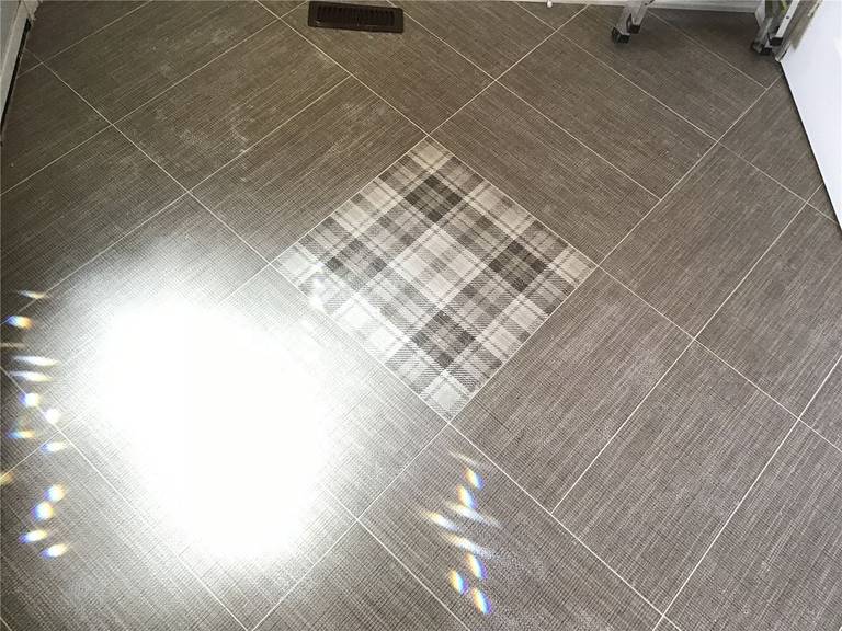 This Woodbridge interior renovation showcases durable grey porcelain floor tiles installed in a clean grid layout, enhanced by a decorative center inlay detail. The design adds visual interest while maintaining a modern and low-maintenance flooring solution, ideal for high-traffic kitchen or living areas.