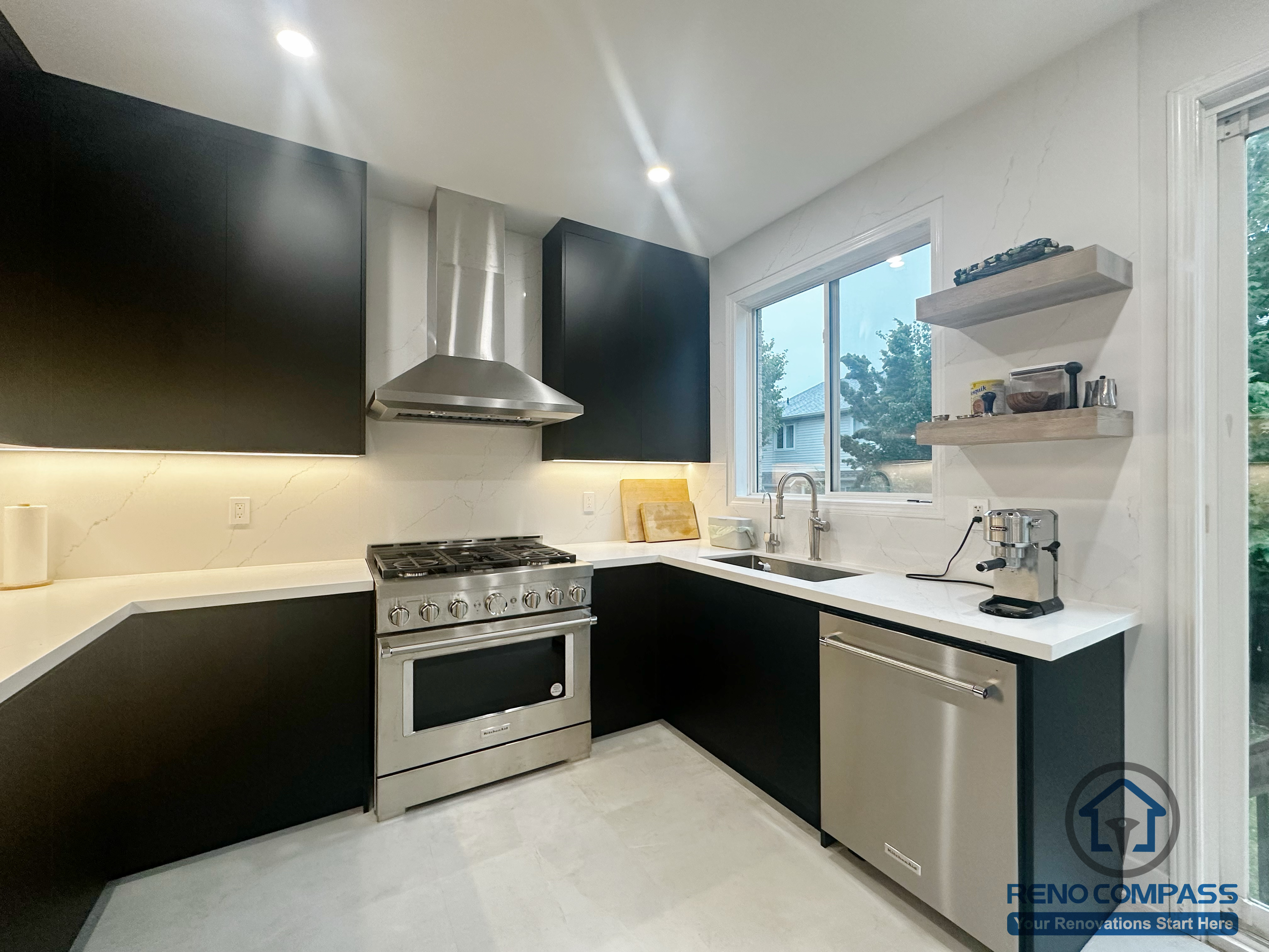 This Oakville kitchen renovation features a clean, modern layout with custom black cabinetry, white quartz countertops, and stainless steel appliances. The U-shaped design maximizes storage and workflow, while open shelving and under-cabinet lighting add both functionality and visual balance. Natural light from the window enhances the bright, minimal aesthetic, creating a practical and timeless kitchen space designed for everyday use.