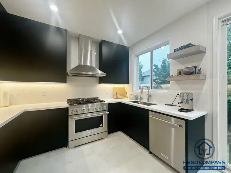 This Oakville kitchen renovation features a clean, modern layout with custom black cabinetry, white quartz countertops, and stainless steel appliances. The U-shaped design maximizes storage and workflow, while open shelving and under-cabinet lighting add both functionality and visual balance. Natural light from the window enhances the bright, minimal aesthetic, creating a practical and timeless kitchen space designed for everyday use.