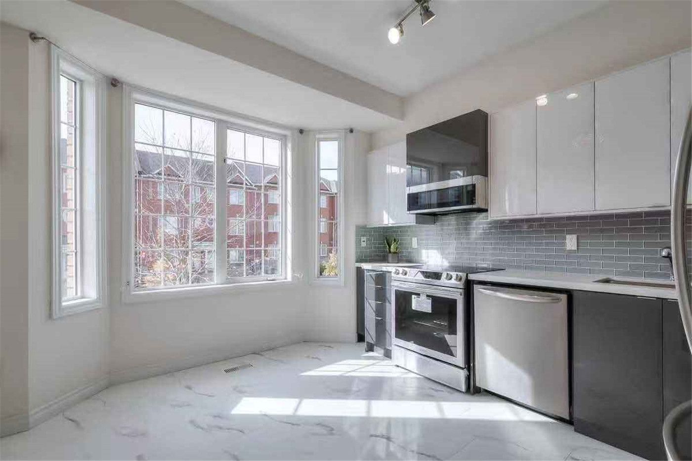 This Thornhill interior renovation showcases a bright and modern kitchen featuring glossy white cabinetry, stainless steel appliances, grey tile backsplash, and elegant marble-style flooring. Large bay windows bring in abundant natural light, enhancing the open and spacious feel of the home. Completed by a professional Toronto renovation team, this upgrade delivers a clean, contemporary interior designed for both comfort and functionality.