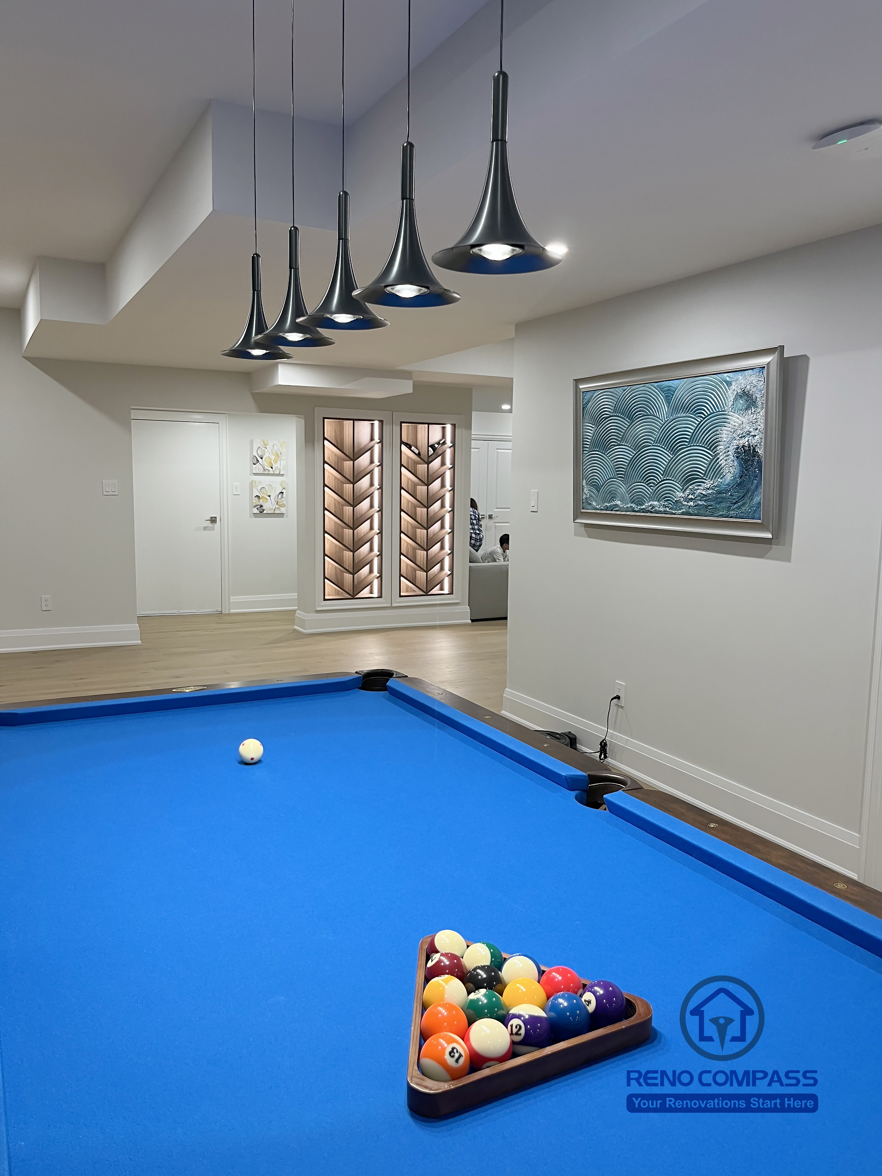 Basement renovation in Newmarket showcasing a pool table area with custom pendant lighting, open-concept layout, and wood flooring, creating a balanced and functional entertainment space.