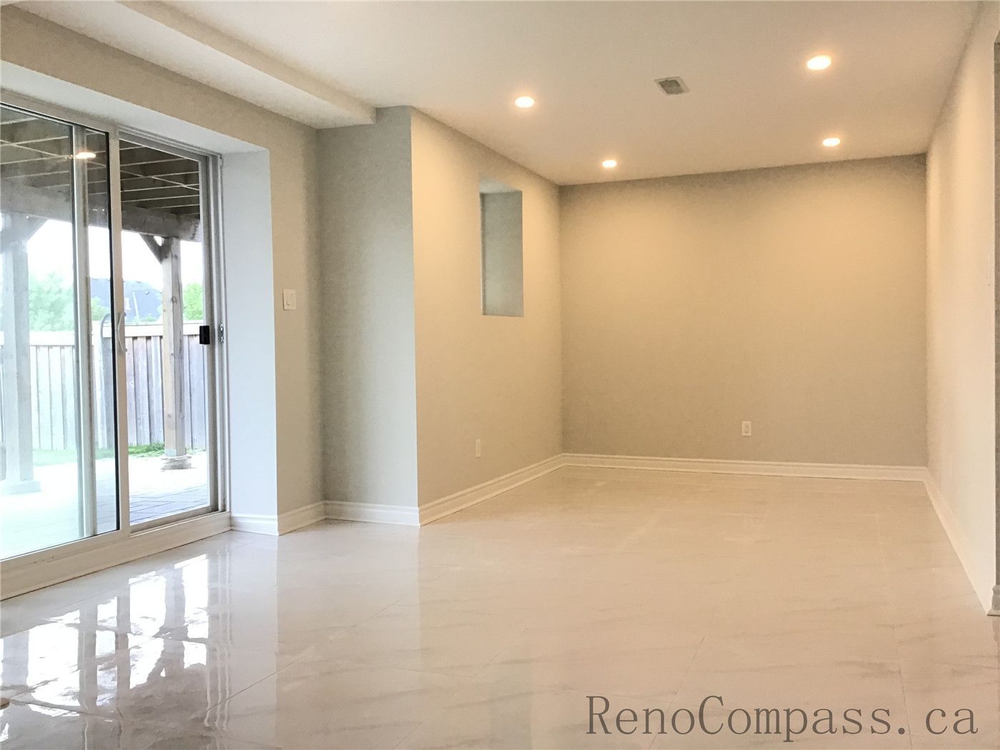 This Whitby basement renovation features a spacious open-concept living area enhanced by large sliding glass doors that bring in natural light and provide direct backyard access. The glossy marble-look porcelain flooring reflects both daylight and recessed ceiling lighting, creating a bright and welcoming atmosphere. Neutral wall tones, clean trim details, and a modern layout make this basement space ideal for a family lounge, entertainment area, or secondary living suite.

Send the next image and I’ll continue formatting them consistently for the project.