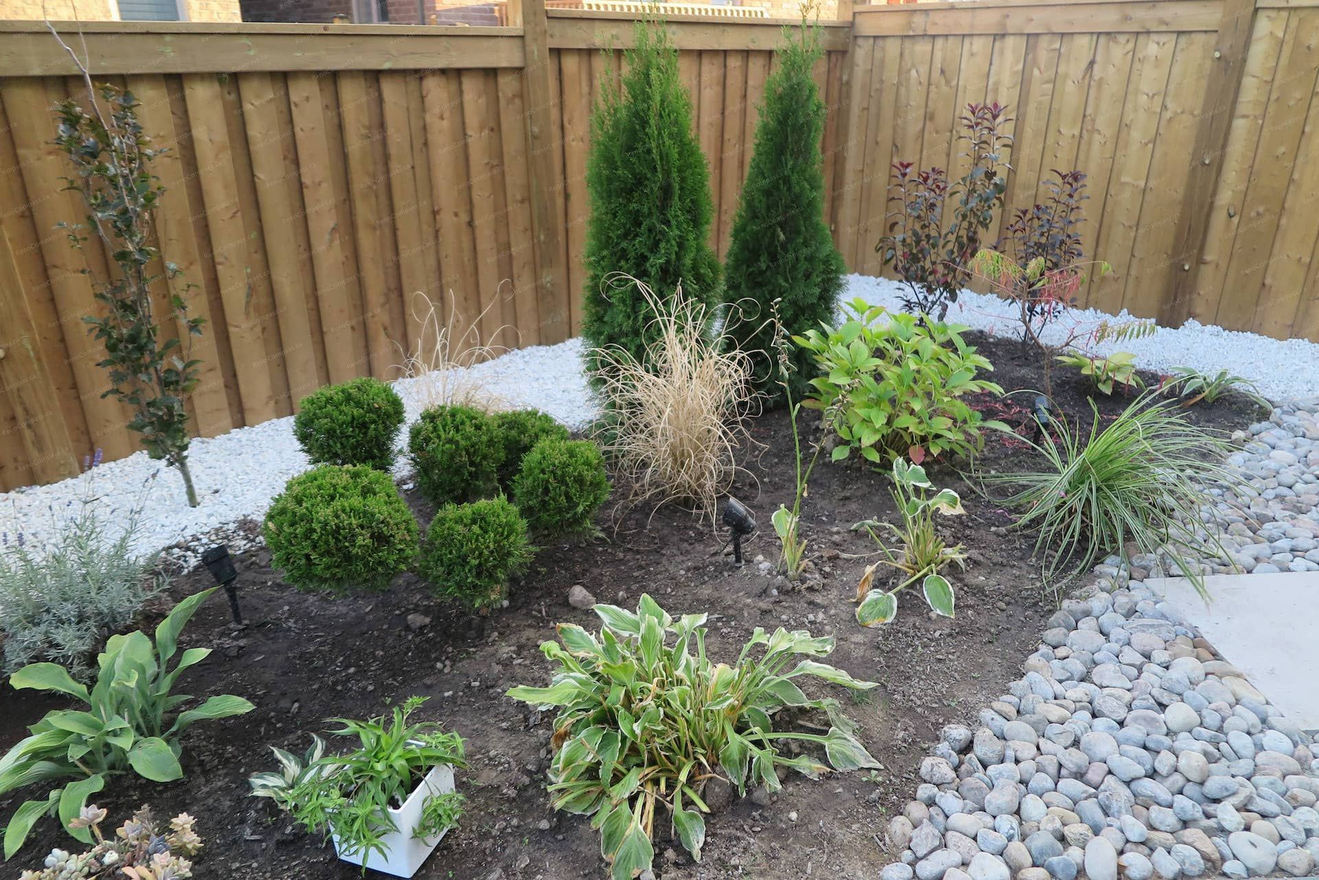 This Vaughan landscaping renovation features a modern interlock patio combined with a carefully arranged garden bed, decorative river rocks, and ornamental plants. The design integrates natural textures, structured greenery, and landscape accents to create a relaxing and visually balanced backyard environment. Professionally completed by Reno Compass Inc.