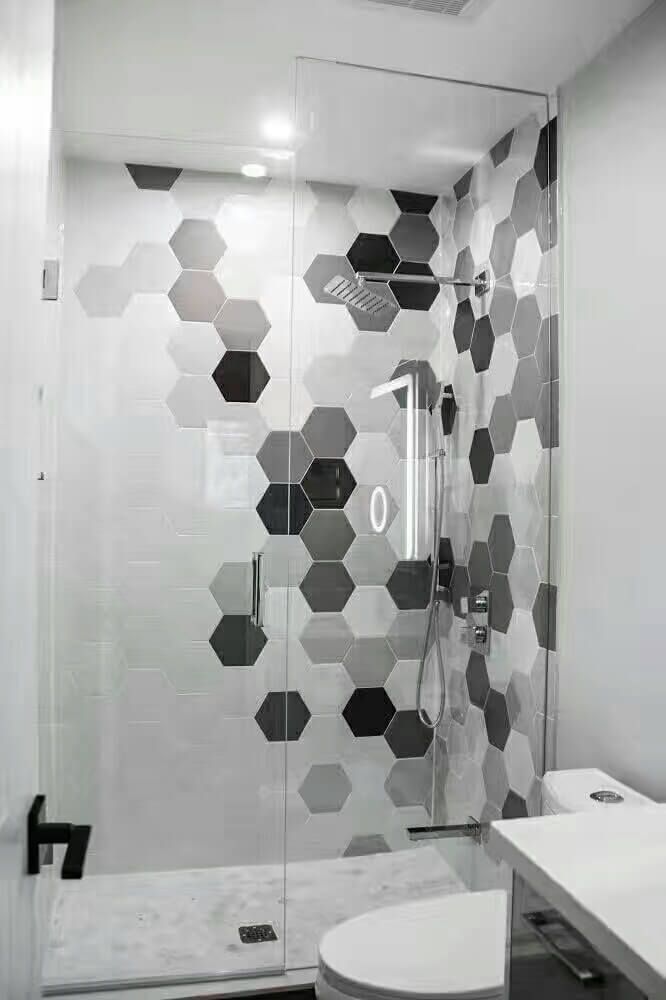 This Markham interior renovation features a modern bathroom upgrade with a custom glass-enclosed shower and striking hexagon tile accent wall. The neutral grey and white tile palette adds visual depth while maintaining a clean, contemporary look. Matte black fixtures, a frameless glass door, and a compact floating vanity maximize functionality in a limited space. Designed for durability and everyday comfort, this bathroom renovation reflects the quality craftsmanship of a professional Toronto renovation contractor.