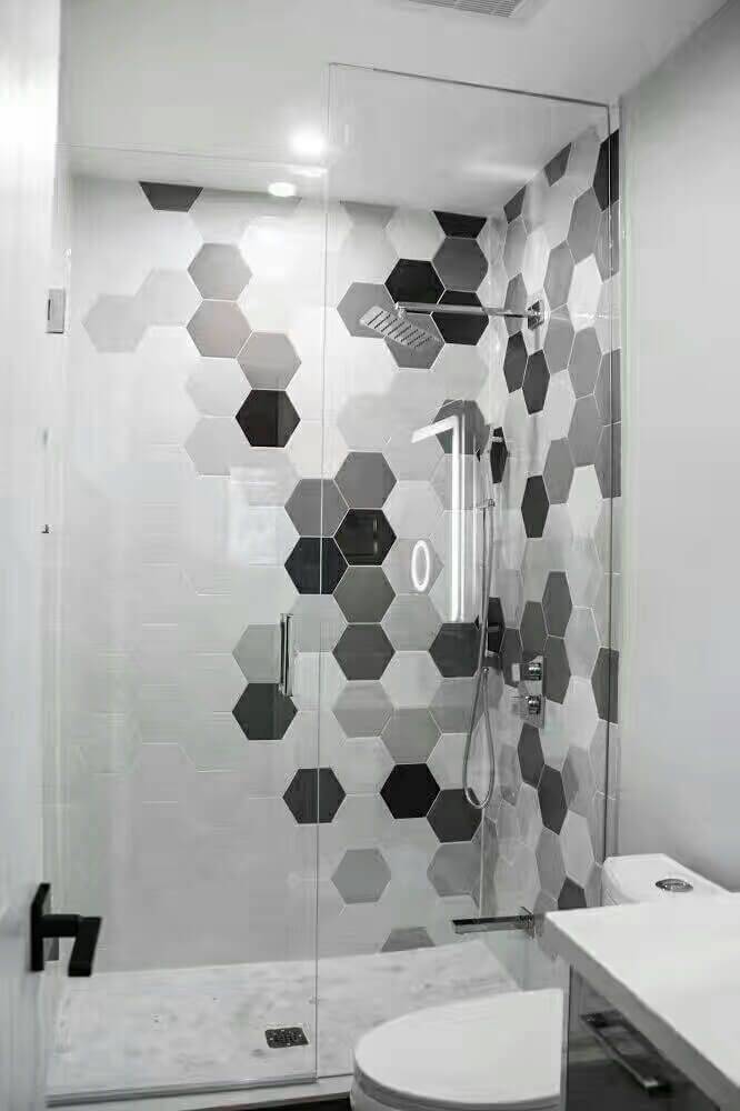 This Markham interior renovation features a modern bathroom upgrade with a custom glass-enclosed shower and striking hexagon tile accent wall. The neutral grey and white tile palette adds visual depth while maintaining a clean, contemporary look. Matte black fixtures, a frameless glass door, and a compact floating vanity maximize functionality in a limited space. Designed for durability and everyday comfort, this bathroom renovation reflects the quality craftsmanship of a professional Toronto renovation contractor.