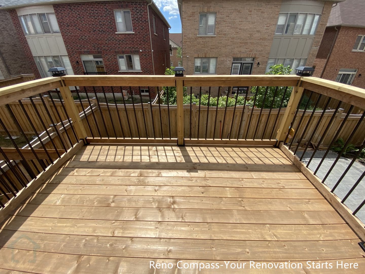 This image showcases the upper-level wooden deck platform completed as part of a Markham outdoor renovation project. The deck features pressure-treated wood decking boards arranged for durability and long-term outdoor performance. Black metal balusters paired with solid wood railings provide a clean, modern look while maintaining safety and structural integrity. The open railing design allows natural light to pass through and preserves clear sightlines across the backyard and surrounding homes. This elevated deck creates a comfortable outdoor space suitable for daily use, entertaining, and seasonal enjoyment. The project was completed by Reno Compass, serving homeowners in Markham and the GTA.