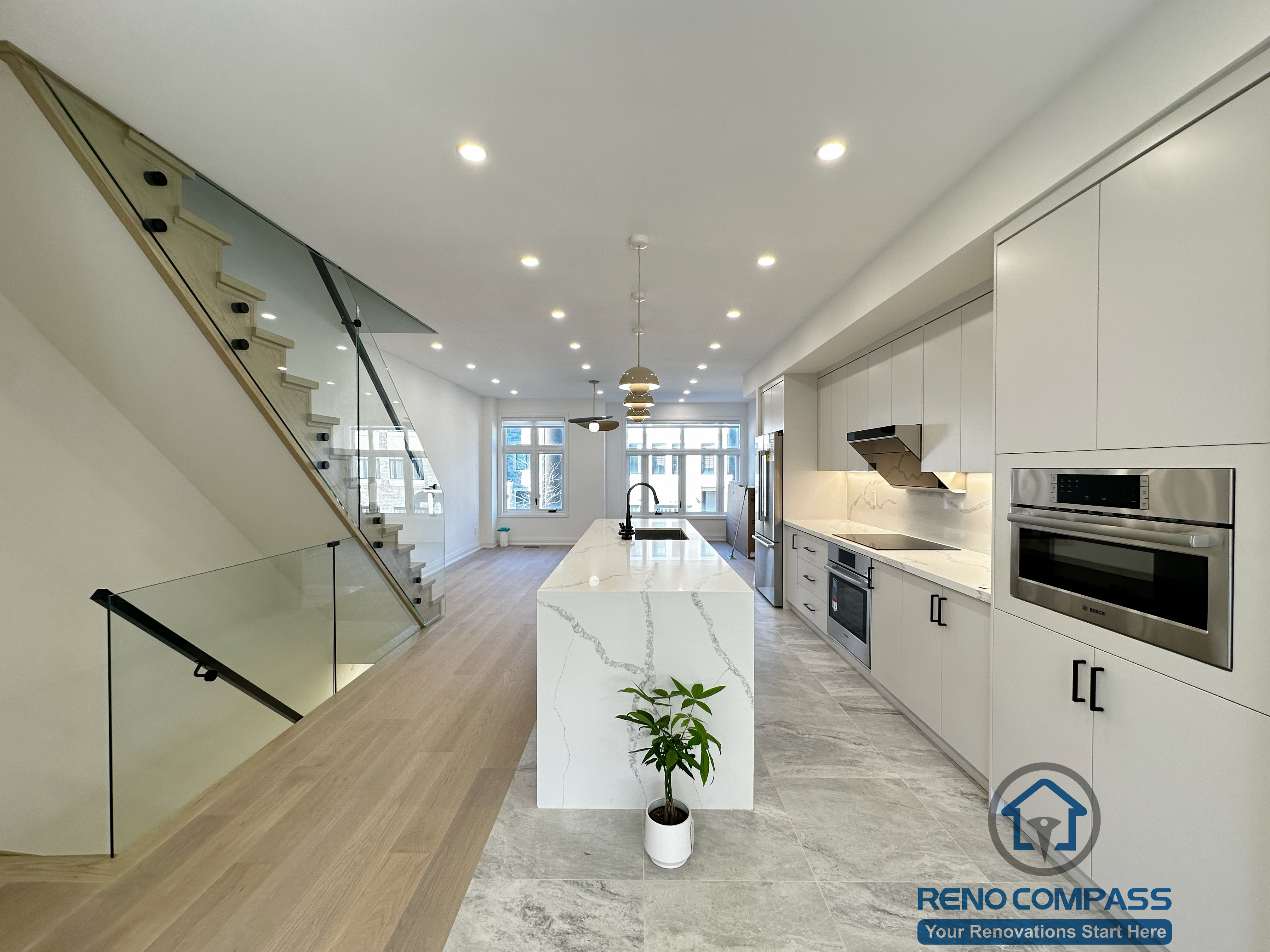 Open-concept kitchen renovation in Richmond Hill featuring a large quartz waterfall island, full-height custom cabinetry, built-in stainless steel appliances, and a seamless transition to the living area. The space is complemented by wide-plank flooring, recessed ceiling lighting, and a modern glass staircase that enhances openness and natural light flow.