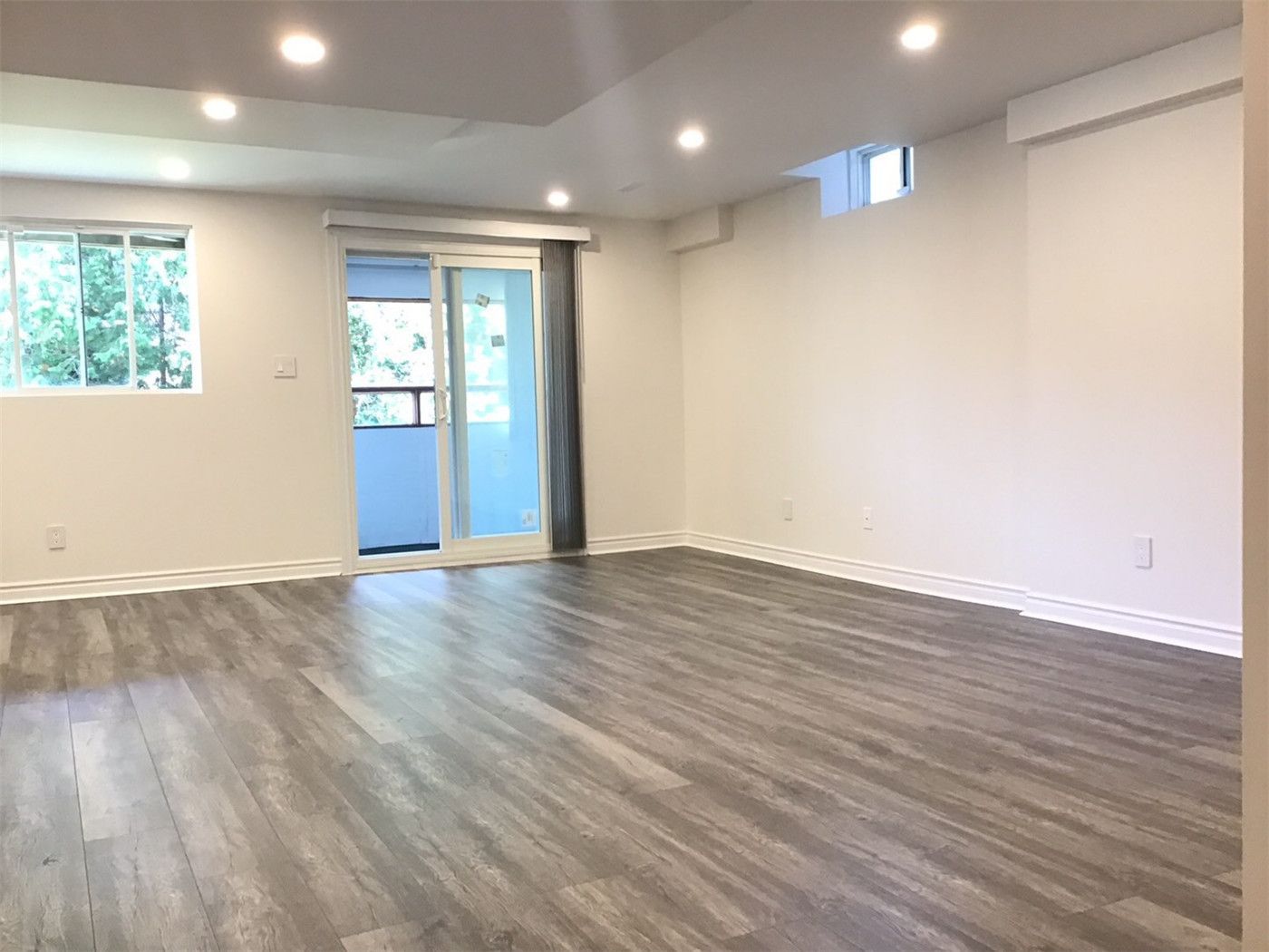 This Richmond Hill basement renovation showcases a bright and spacious open-concept layout featuring durable wood-look vinyl flooring, recessed pot lights, and clean white walls. The large sliding door and windows bring in natural light, creating a comfortable and functional living space ideal for family use or rental potential. A great example of modern basement finishing in Richmond Hill.