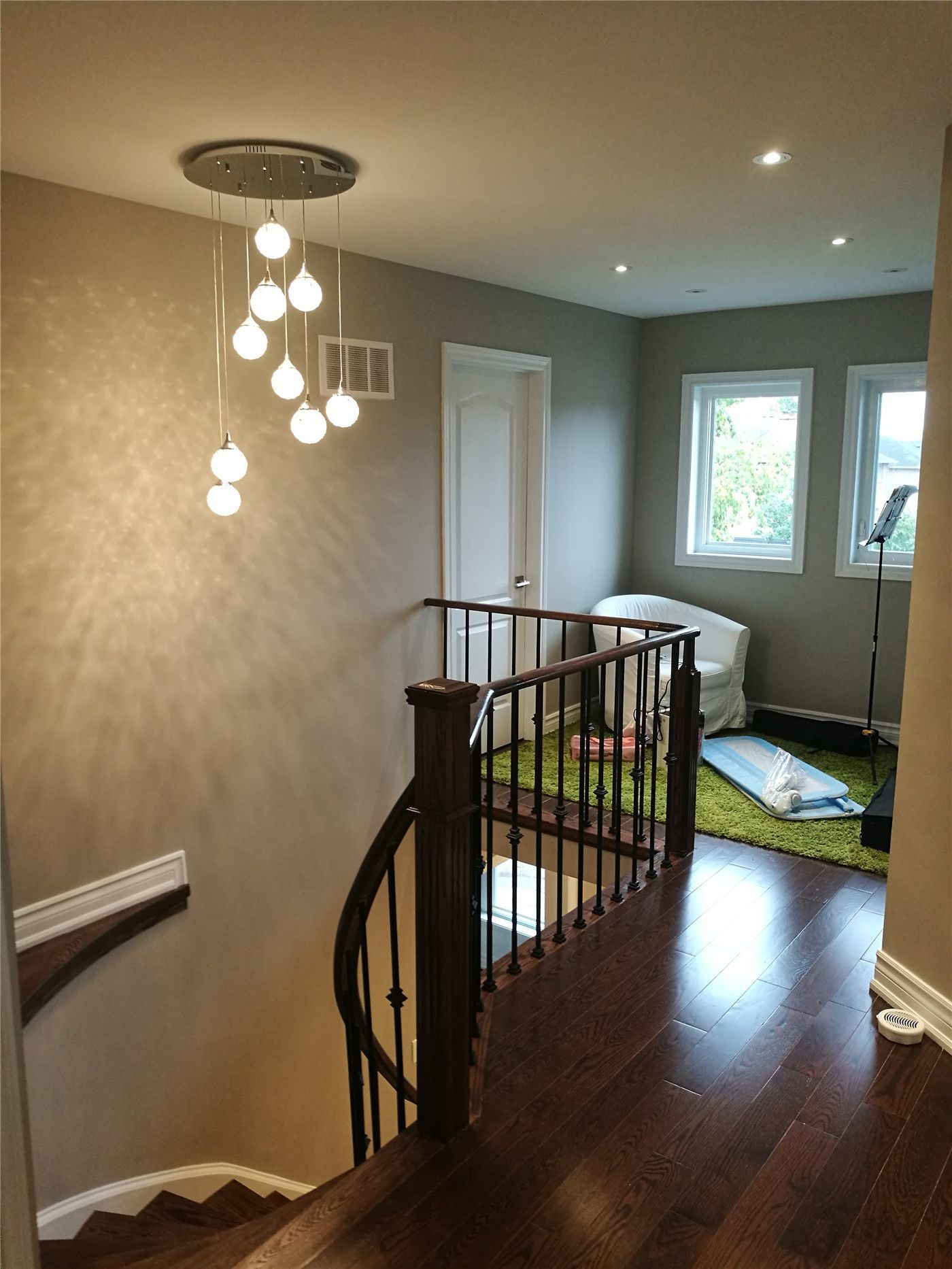 This Newmarket interior renovation features a refined staircase and upper hallway finished with dark hardwood flooring, custom railing, and a modern multi-pendant chandelier. Recessed ceiling lights and soft neutral wall tones enhance brightness and depth, demonstrating the attention to detail and interior craftsmanship of a professional Toronto renovation company.