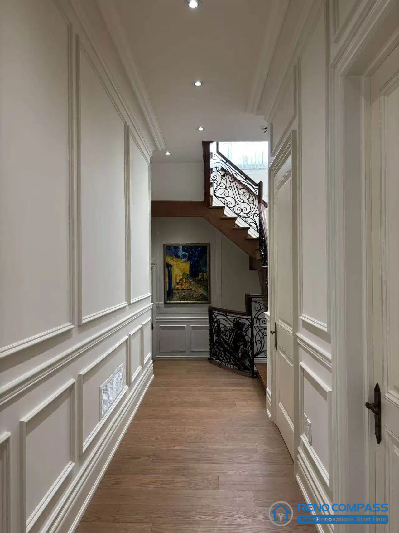 This image features a European-style hallway defined by classical wall panelling, balanced proportions, and a clear circulation axis leading toward the staircase. Full-height panels and consistent trim detailing establish rhythm and order along the corridor, while recessed lighting supports a calm and structured passage. The transition toward the staircase introduces wrought iron detailing and layered depth, reinforcing architectural continuity between levels. Hardwood flooring grounds the space and aligns visually with adjacent rooms. This view highlights disciplined spatial planning and refined detailing within a high-end Richmond Hill interior renovation.