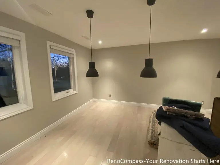 This finished dining area features light wood flooring, neutral wall finishes, and minimalist pendant lighting that defines the space without visual clutter. Large windows bring in natural light, enhancing brightness and creating a comfortable setting for daily dining and gathering. Designed and completed by Reno Compass, this renovation balances clean proportions, practical lighting layout, and long-term everyday use.