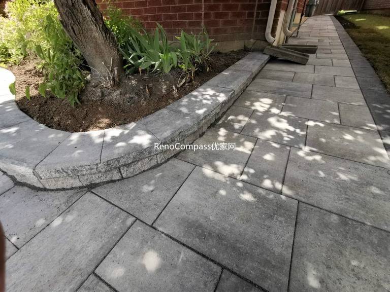 Beautifully finished side walkway interlocking project in Richmond Hill. The light gray stone pavers are neatly aligned against the house, featuring a raised garden border for a clean and modern look. Installed by Reno Compass for improved drainage, durability, and curb appeal.
