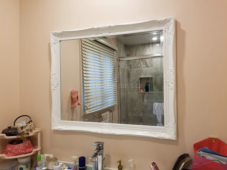 This Markham bathroom renovation showcases a newly updated vanity area paired with a decorative framed mirror that enhances the brightness and visual space of the bathroom. The mirror reflects the upgraded shower with new wall tiles and built-in niche, highlighting the cohesive design of this full bathroom remodel. The renovation delivers improved functionality, elegant finishes, and a refreshed modern look for everyday comfort.