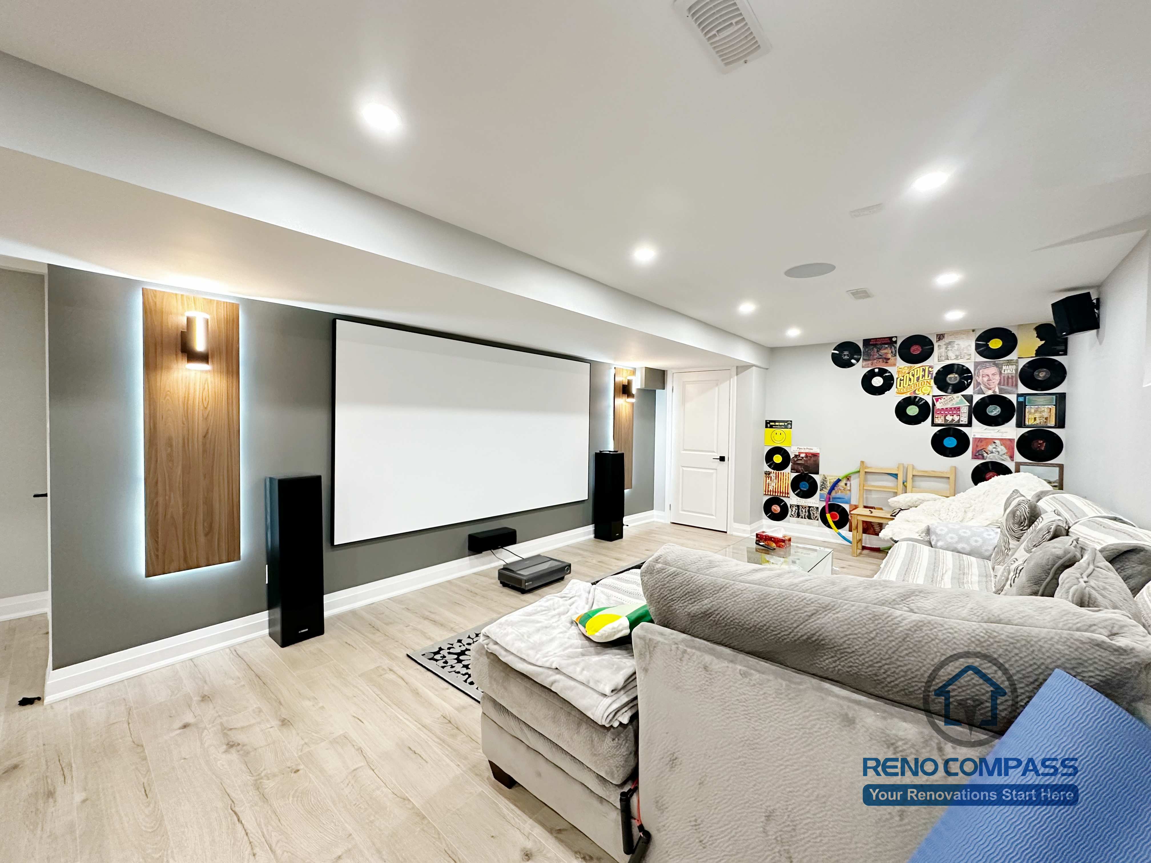 This Newmarket basement renovation features a custom home theater with a built-in projector screen, accent wall lighting, and integrated speaker placement. The finished basement is designed as a multifunctional family entertainment space, combining a modern media wall, comfortable seating area, and durable flooring for everyday use and movie nights.