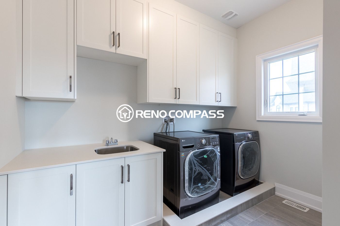 Functional laundry room renovation in Newmarket featuring custom white cabinetry, built-in sink, and raised washer and dryer platform. Completed by a professional Toronto renovation company, this design maximizes storage and creates a clean, organized laundry space.