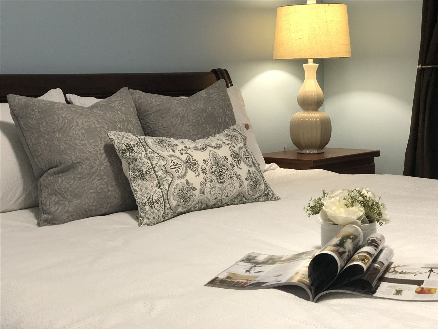 This Toronto interior design pre-sale staging highlights a beautifully styled bedroom with neutral bedding, layered accent pillows, and warm bedside lighting. The soft color palette, decorative cushions, and carefully arranged décor create a calm and inviting atmosphere.
