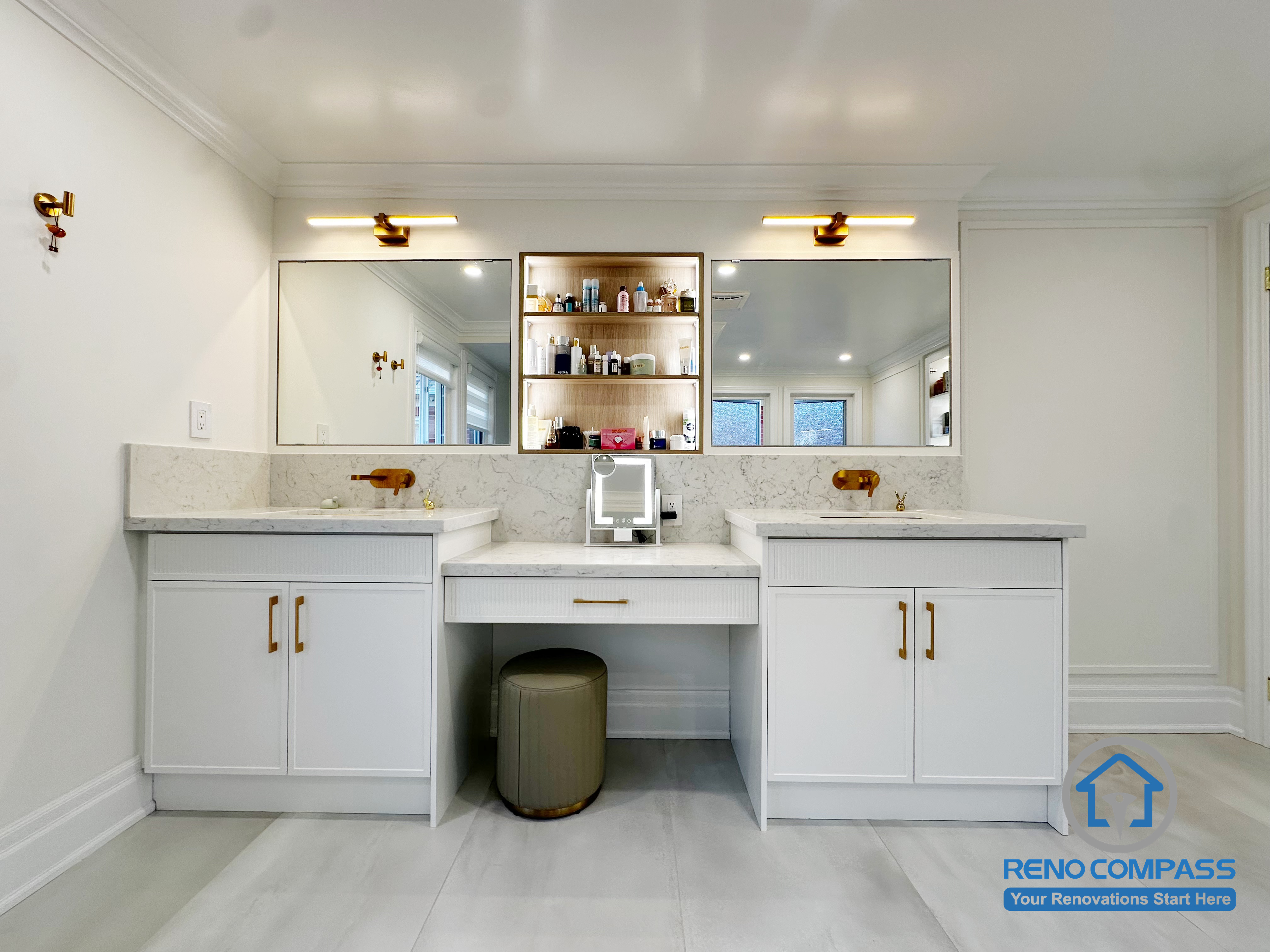 This Markham bathroom renovation features a symmetrical double vanity layout with a dedicated central makeup area, designed to improve daily usability and shared routines. Custom cabinetry provides balanced storage on both sides, while integrated lighting and warm metal accents add a refined, cohesive look. The clean white palette, combined with thoughtful proportions and functional zoning, creates a bathroom space that feels bright, organized, and tailored for everyday comfort.