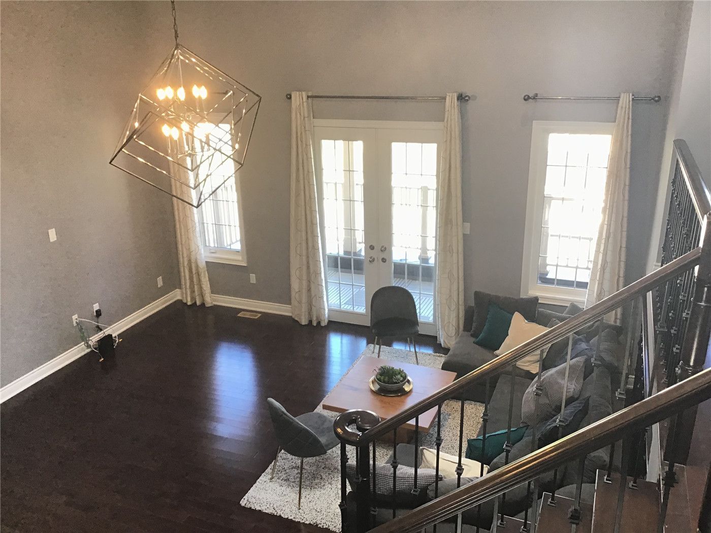 This Markham full home renovation showcases a bright and elegant living room featuring high ceilings, modern geometric chandelier lighting, and dark hardwood flooring. The space is enhanced with large windows and French doors that bring in natural light, creating a warm and inviting atmosphere. Designed and completed by a professional Toronto Renovation Company, this project highlights both functionality and contemporary aesthetics.