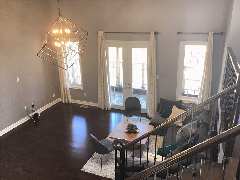 This Markham full home renovation showcases a bright and elegant living room featuring high ceilings, modern geometric chandelier lighting, and dark hardwood flooring. The space is enhanced with large windows and French doors that bring in natural light, creating a warm and inviting atmosphere. Designed and completed by a professional Toronto Renovation Company, this project highlights both functionality and contemporary aesthetics.
