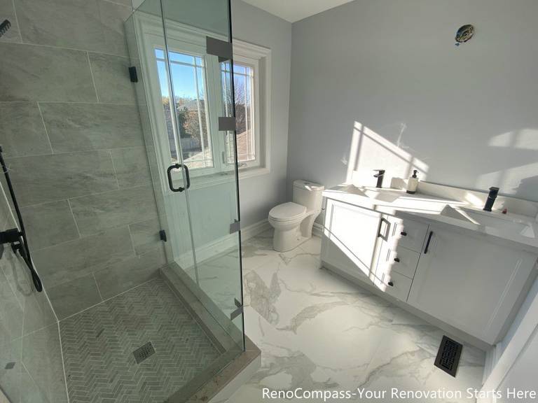 This Thornhill bathroom renovation presents a bright and well-balanced layout featuring a frameless glass walk-in shower, a modern vanity, and a large window that brings in abundant natural light. The herringbone-patterned shower base adds visual texture, while marble-look porcelain flooring enhances continuity throughout the space. Matte black fixtures provide subtle contrast, creating a clean, functional bathroom designed for daily use, comfort, and long-term durability.