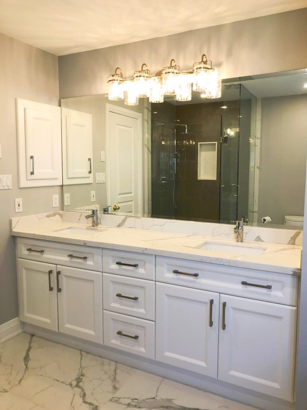 This Richmond Hill bathroom renovation features a modern double-sink vanity with custom white shaker cabinetry, quartz countertops, and sleek black hardware. The upgraded layout improves both storage and daily functionality while maintaining a clean and timeless aesthetic. Large-format marble-style flooring and a glass shower enclosure enhance the luxury feel, creating a bright and elegant space ideal for modern family living. Professionally completed by a trusted Toronto renovation company, this project combines durability, comfort, and refined design for long-term use.