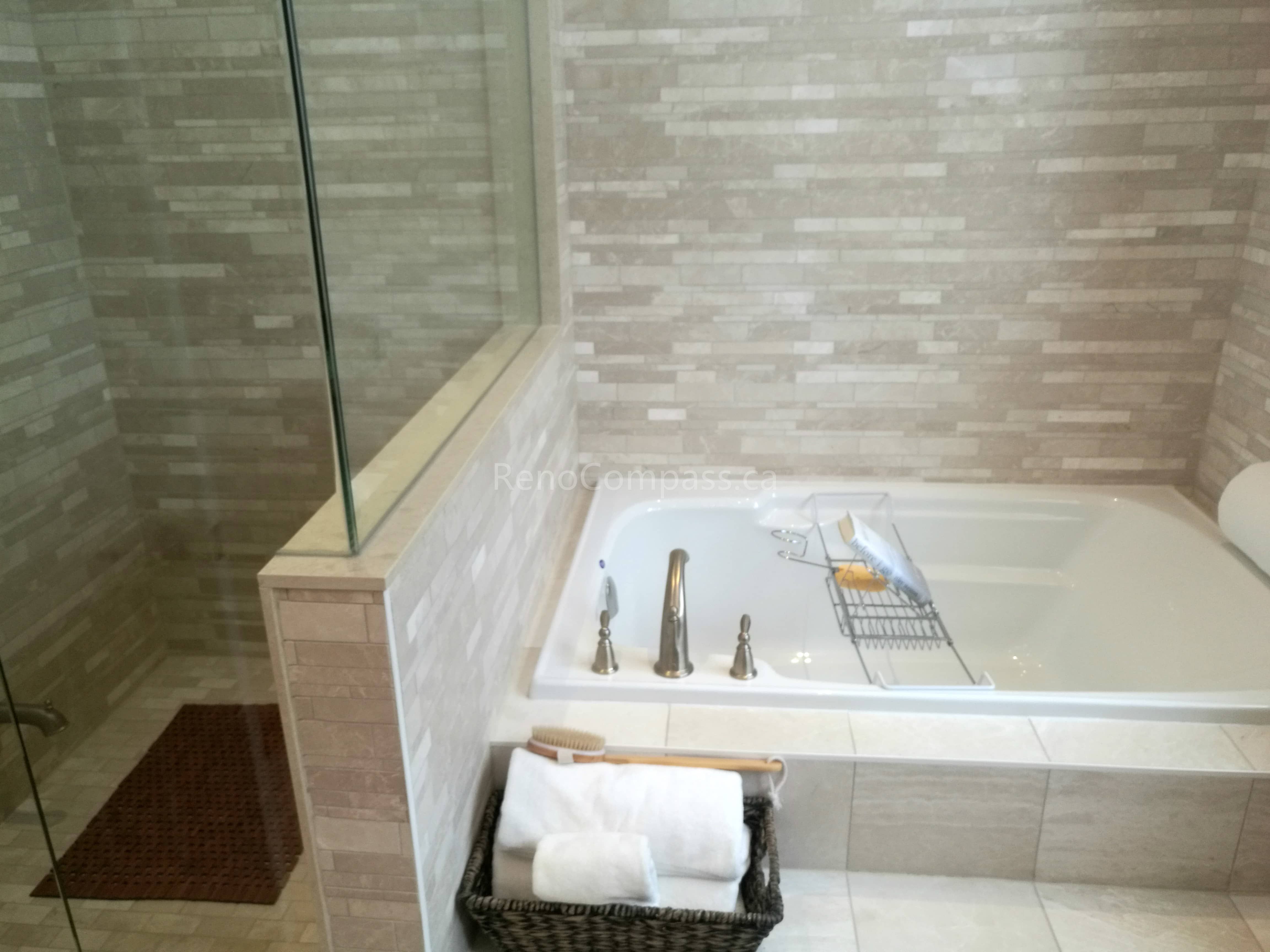 This image showcases a modern bathroom completed as part of a Toronto interior renovation project. The space features a built-in soaking tub paired with a glass-enclosed shower, creating a clean and functional layout. Neutral-toned tile finishes add texture and warmth, while the frameless glass panel enhances openness and visual continuity. Carefully selected fixtures and practical storage details contribute to a calm, spa-like atmosphere. This bathroom renovation highlights quality craftsmanship and thoughtful material selection tailored to contemporary Toronto homes.